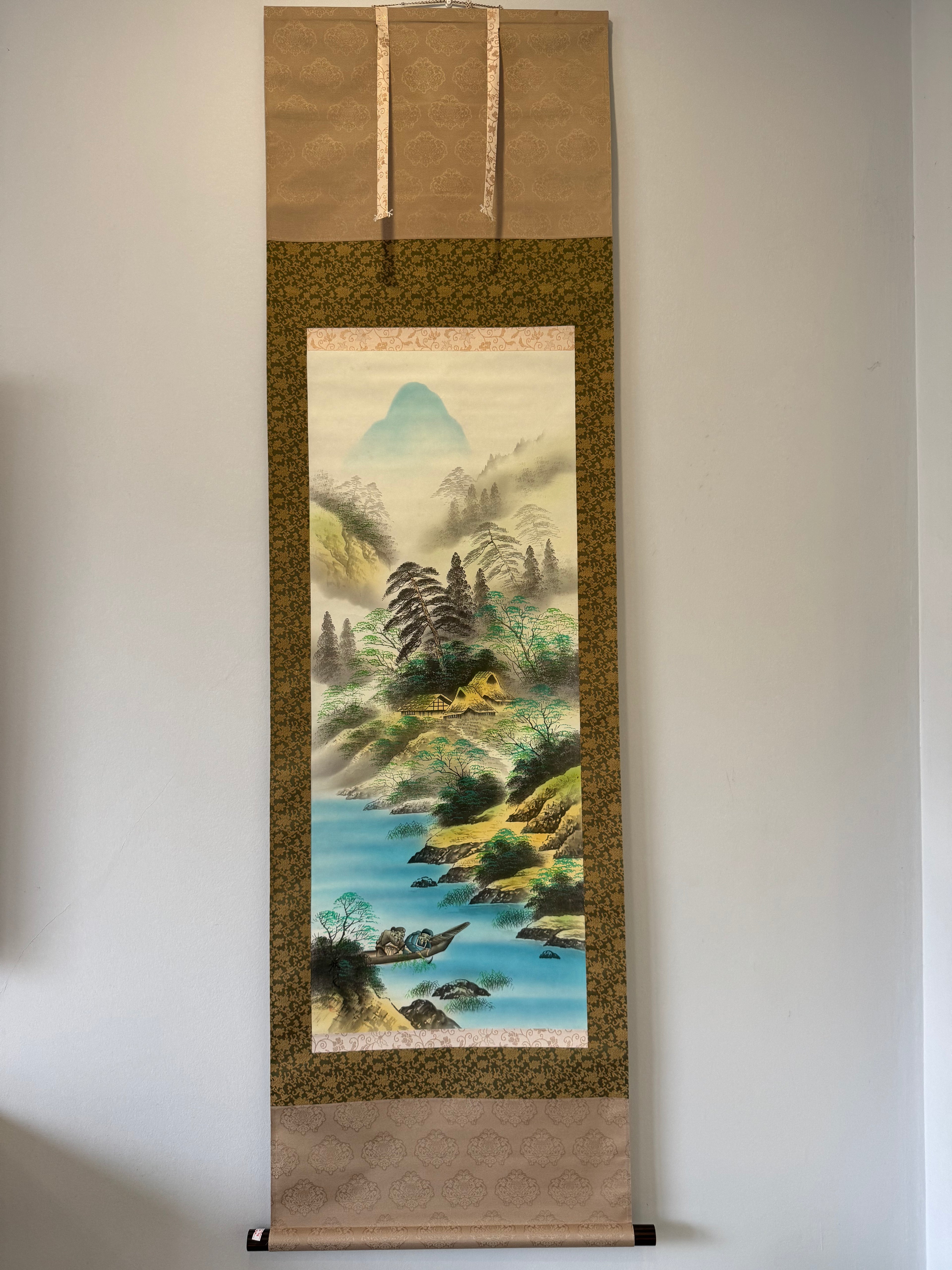 Traditional Japanese landscape scroll with mountains and a lake on a plain wall.