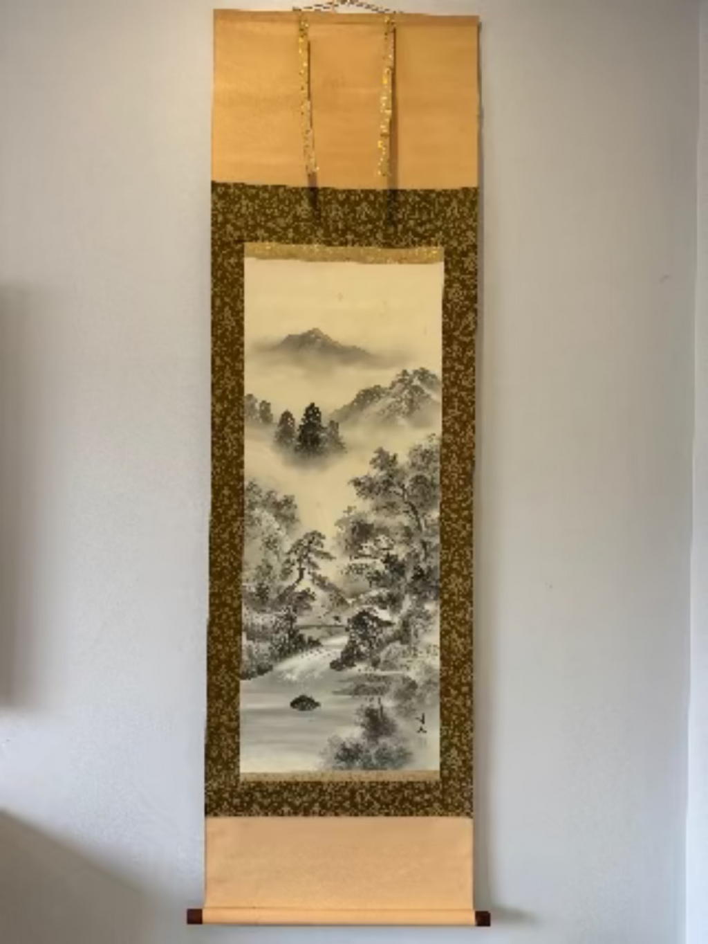 Traditional Chinese landscape painting in a vertical scroll frame on a plain wall.