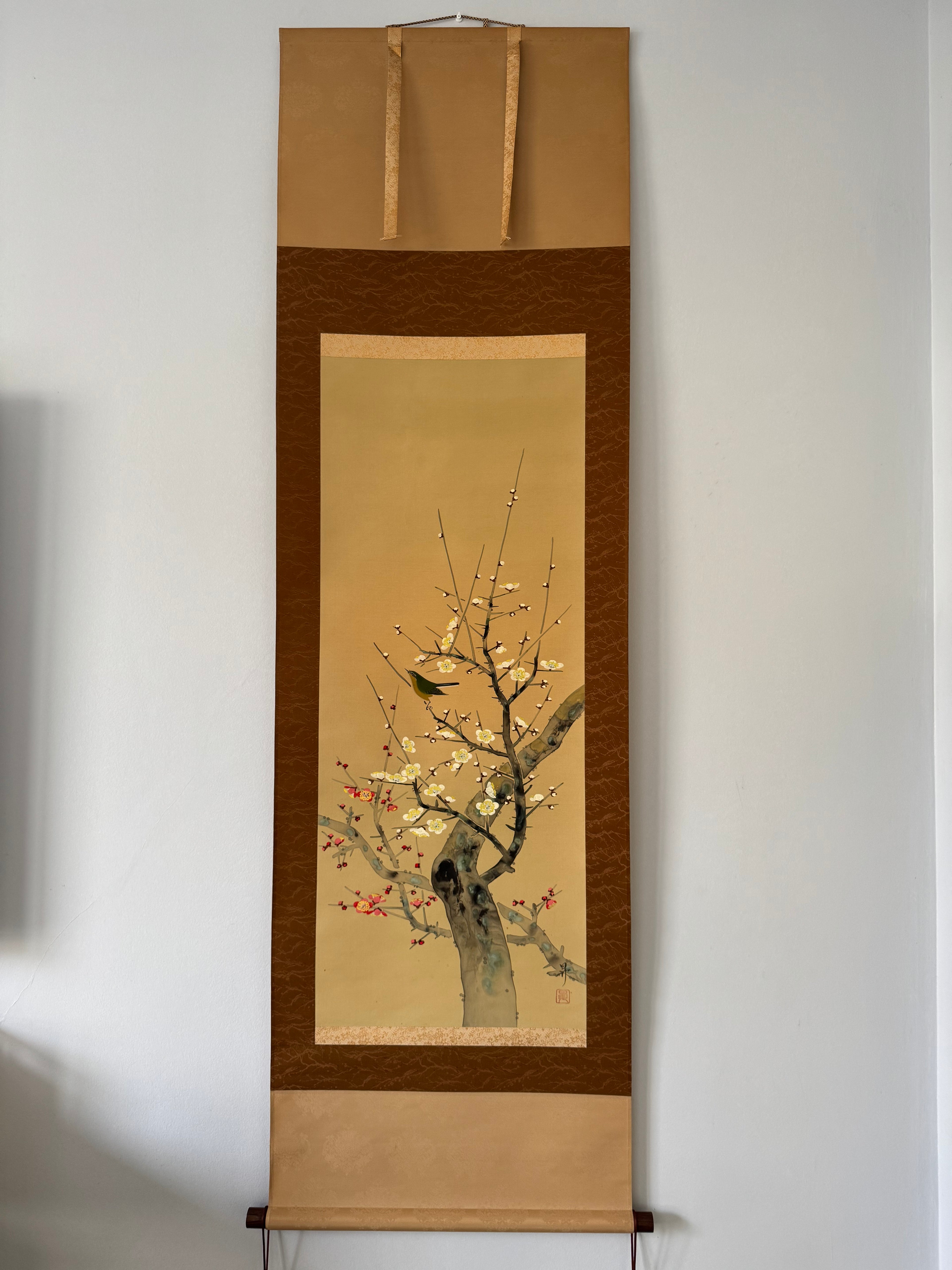 Traditional Japanese hanging scroll with a tree design on a plain wall.