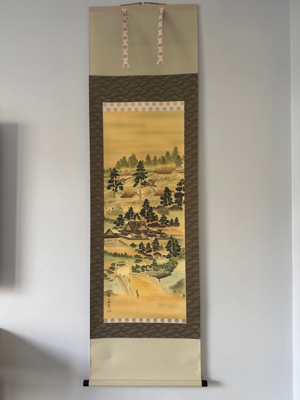 Traditional Japanese landscape painting in a vertical scroll on a plain wall.