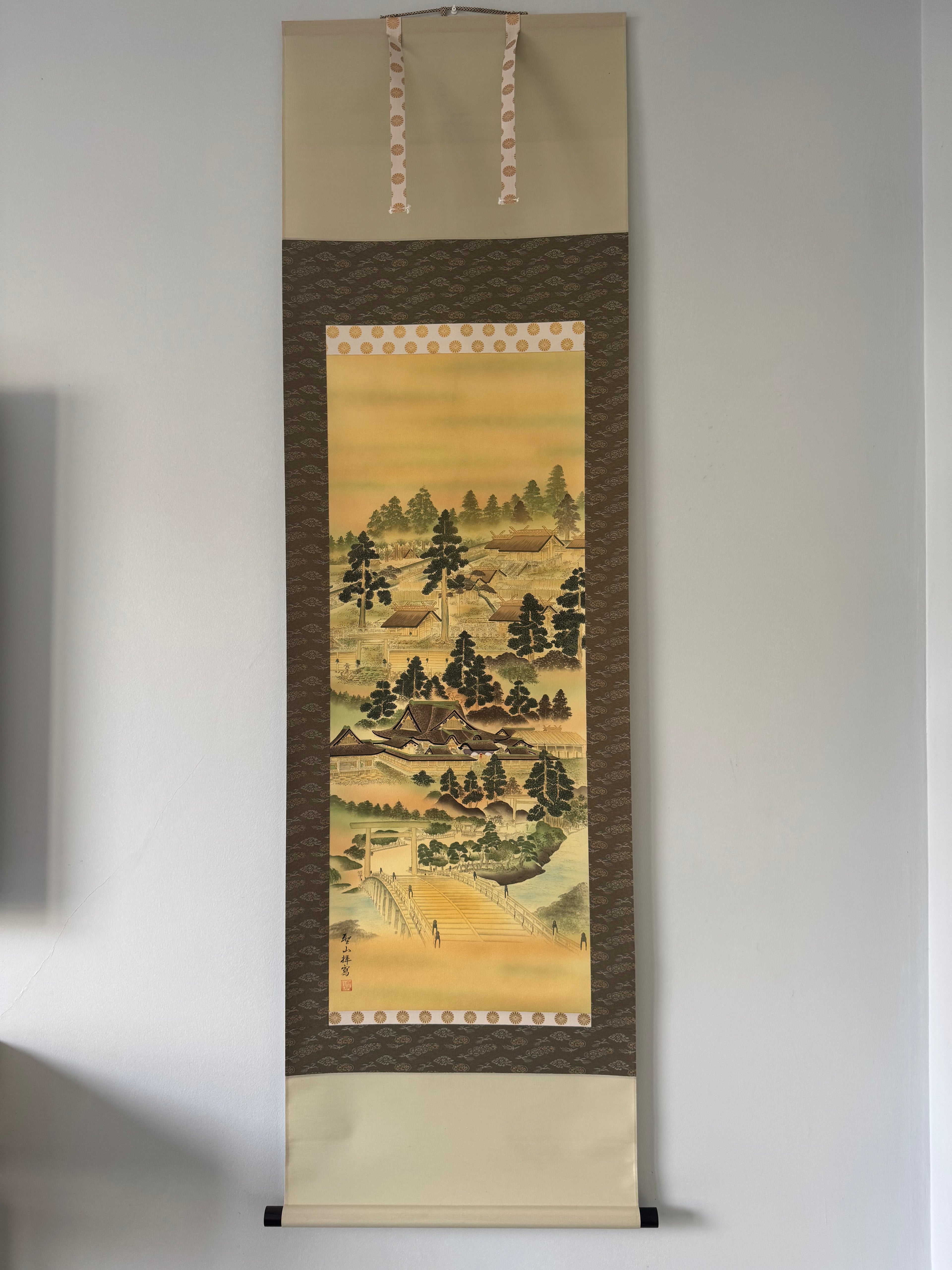 Traditional Japanese landscape painting in a vertical scroll on a plain wall.