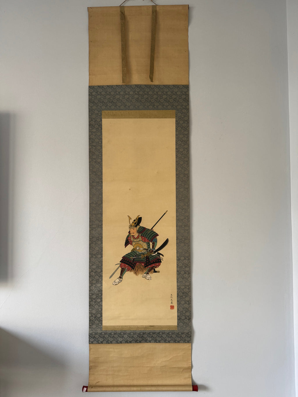 Traditional Japanese scroll with a warrior illustration on a plain wall.
