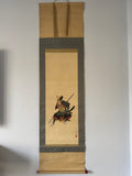Traditional Japanese scroll with a warrior illustration on a plain wall.