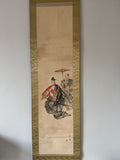 Traditional Japanese artwork on a vertical scroll with a gold border, featuring two figures in formal attire.
