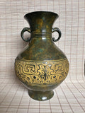 An antique-style bronze vase with a dark green patina and gold-colored Chinese dragon motifs, featuring two side handles, set against a beige woven mat background.