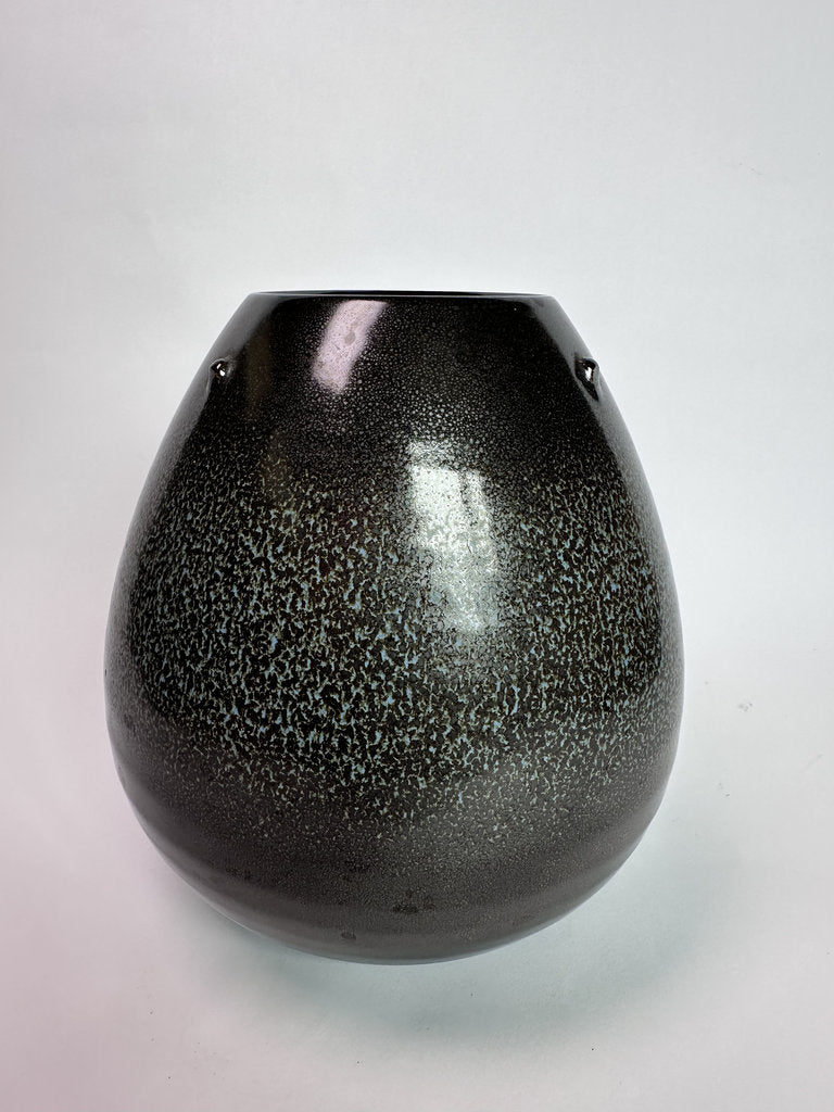 A glossy black ceramic vase with a fine silver speckled glaze, featuring two small metal loop handles on the sides, set against a plain light gray background.