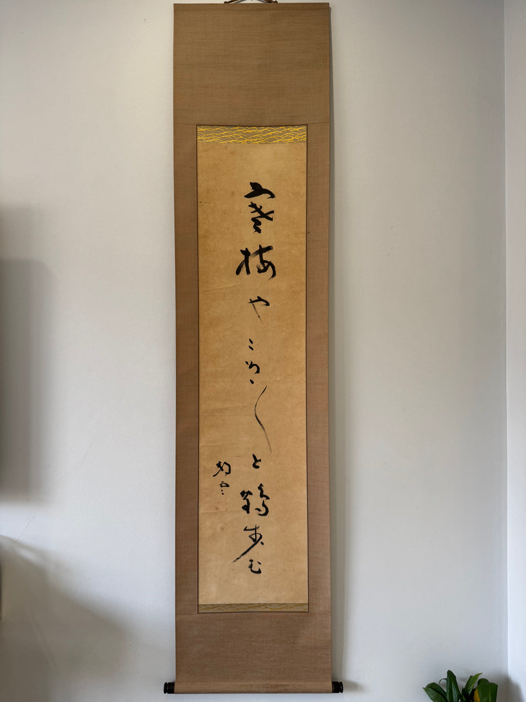 Vertical scroll with calligraphy on a wooden frame against a white wall