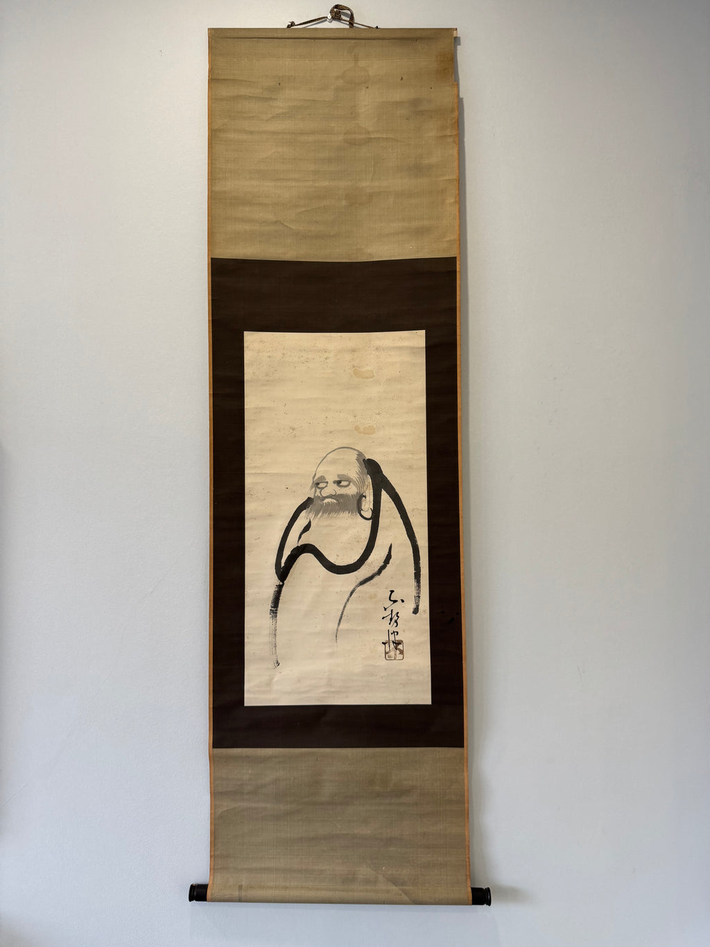 Traditional Japanese scroll with a portrait on a plain wall