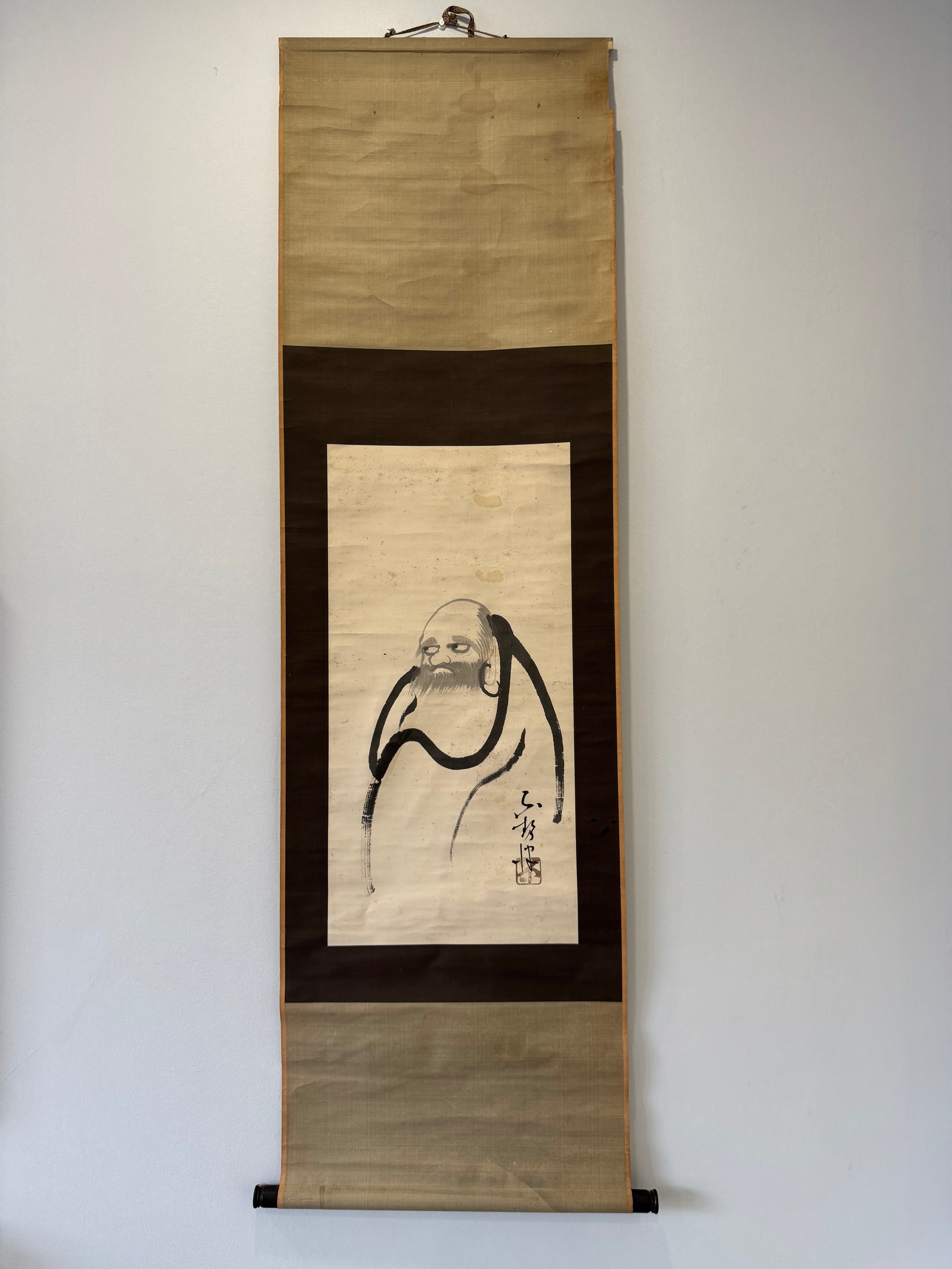 Traditional Japanese scroll with a portrait on a plain wall
