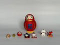 Set of small decorative figurines in front of a larger red and gold figurine on a gray background