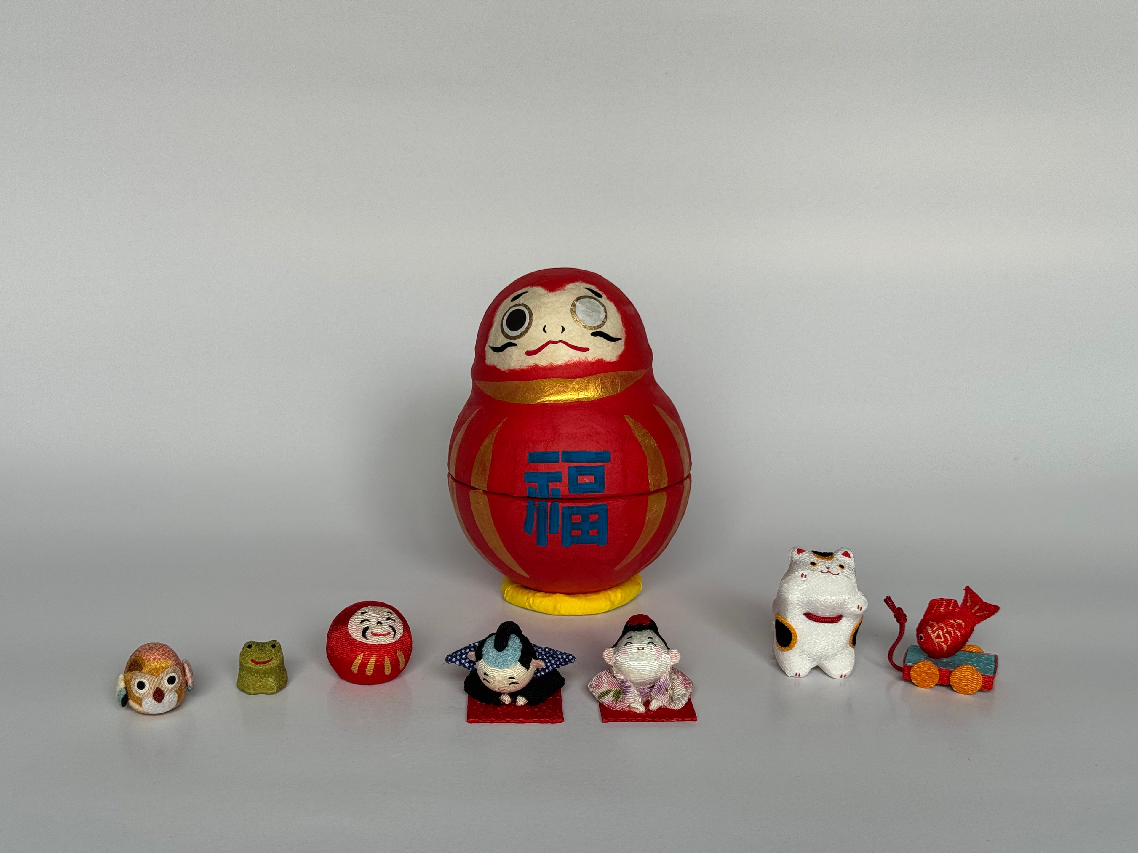 Set of small decorative figurines in front of a larger red and gold figurine on a gray background