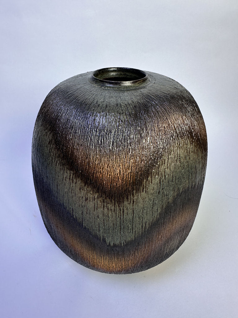 A textured ceramic vase with a rounded, bulbous shape and a narrow cylindrical opening. The surface features a metallic, brushed finish with wavy bands of dark bronze, brown, and a muted olive-green glaze, set against a plain light gray background.