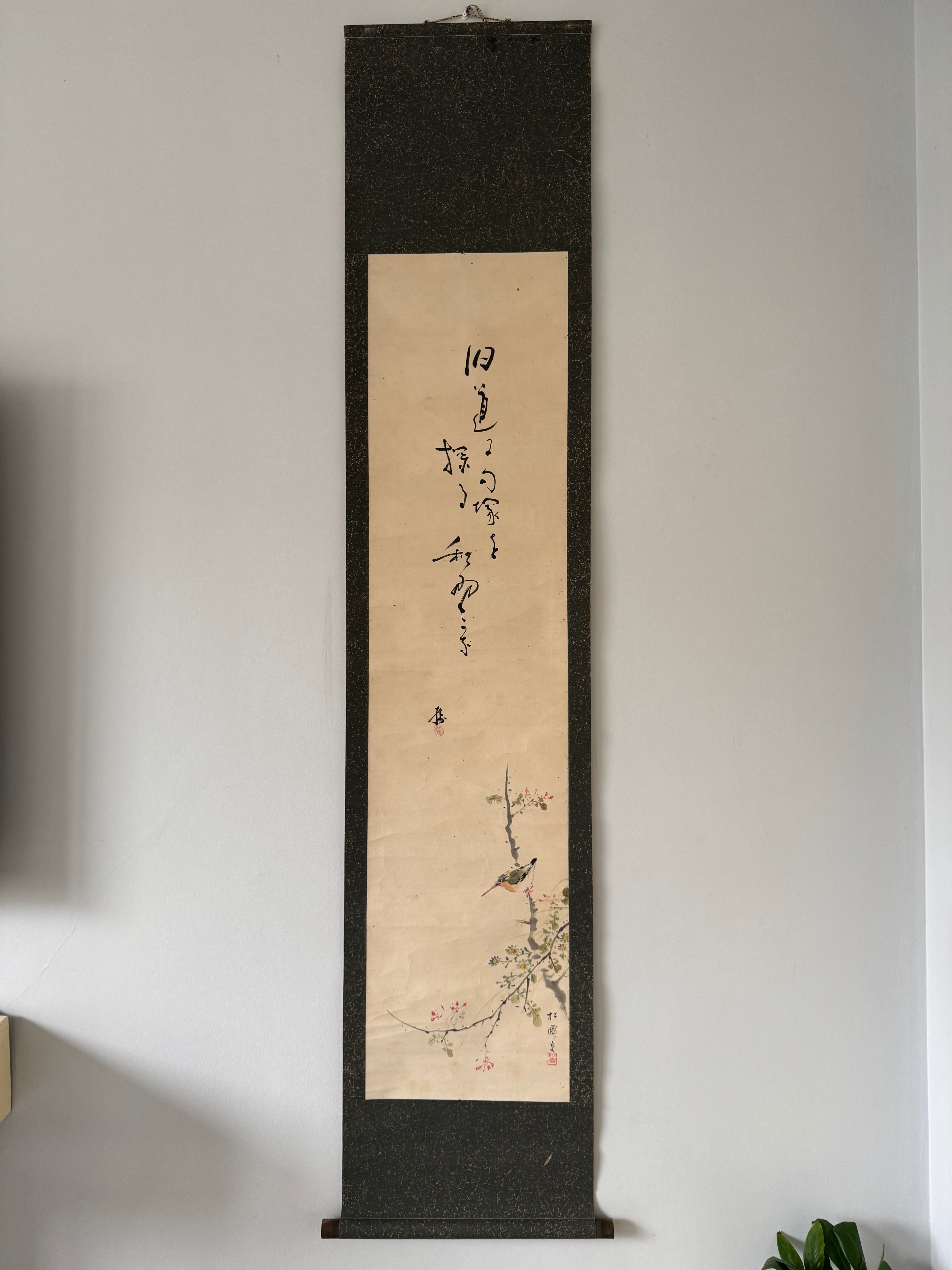 Vertical scroll with calligraphy and floral design on a plain wall