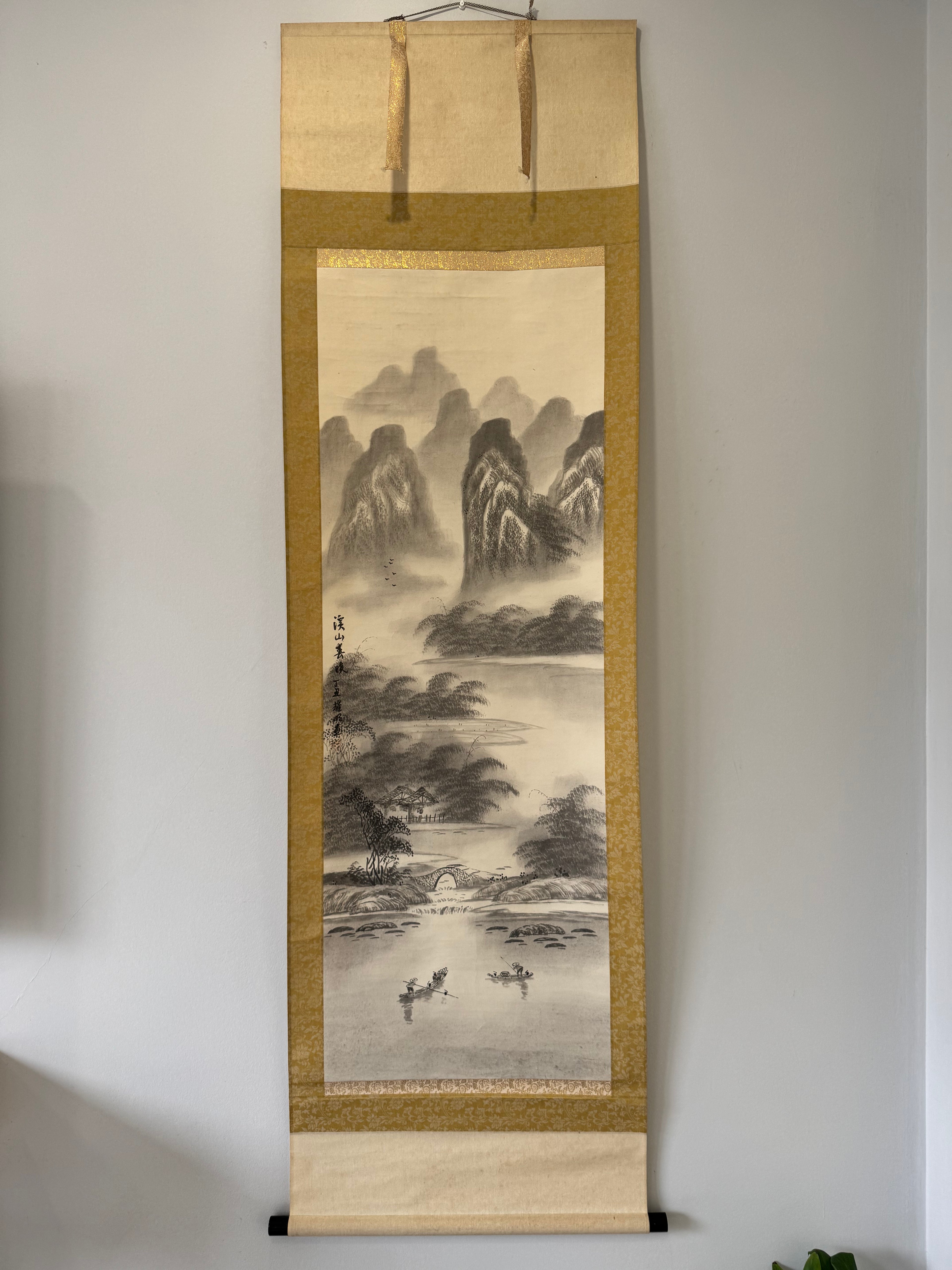 Traditional landscape painting in a vertical scroll on a plain wall.