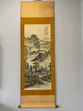 Traditional landscape painting on a vertical scroll against a plain wall.