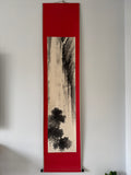 Vertical artwork with black ink design on beige paper, framed in red, against a white wall.