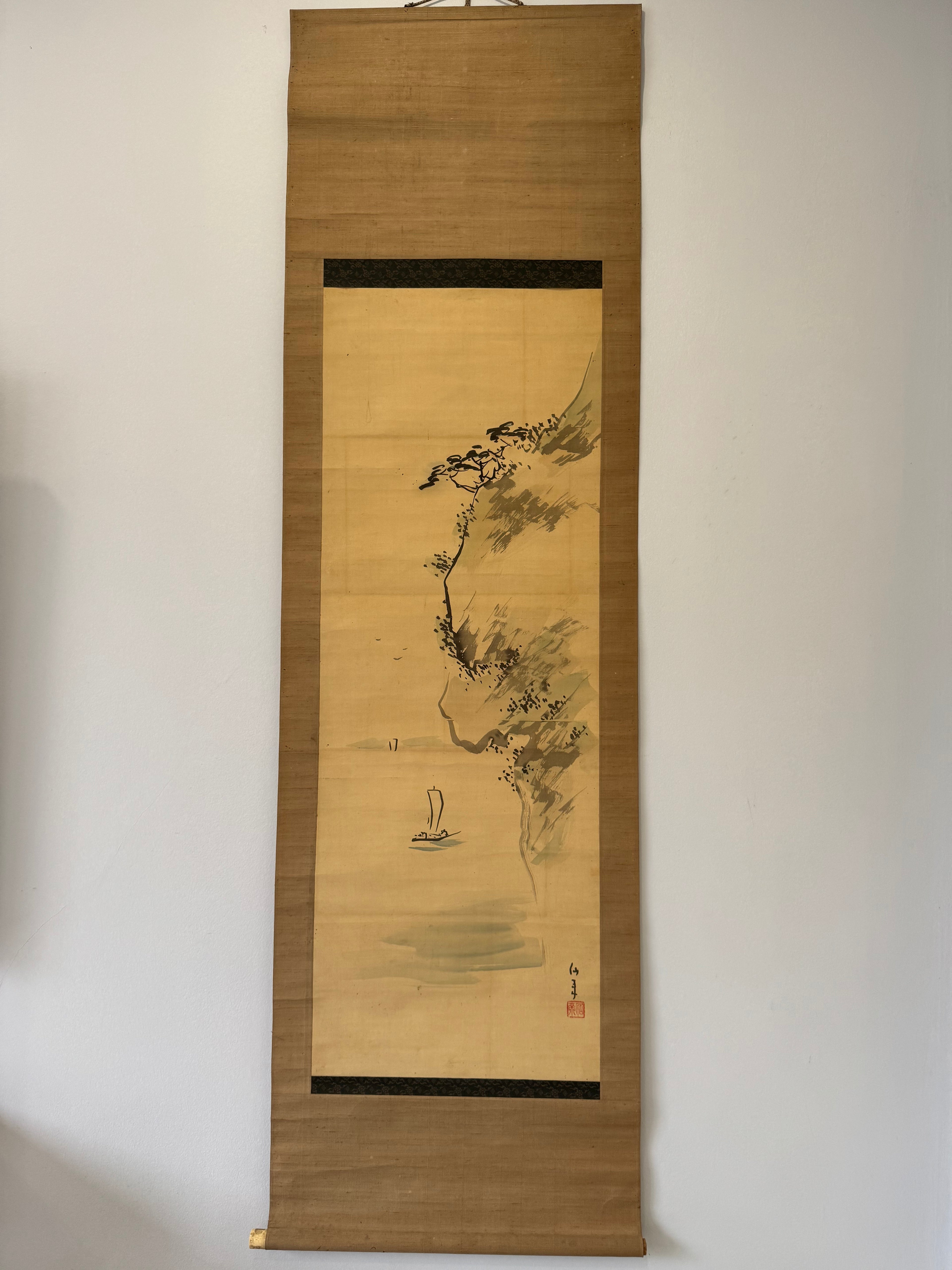 Traditional Japanese hanging scroll with a landscape scene on a plain wall.