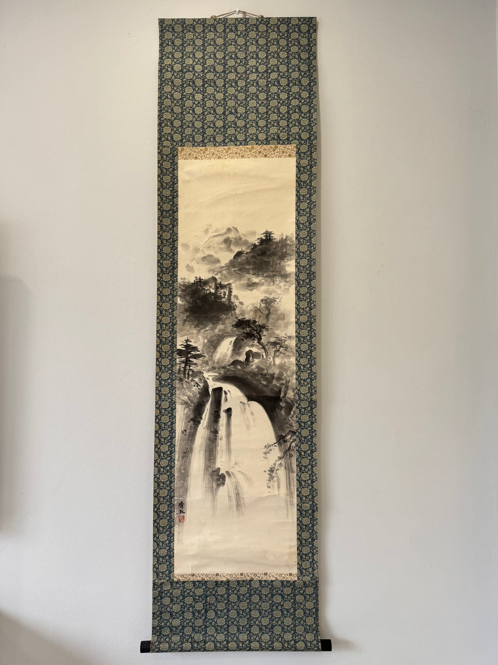 Traditional Japanese landscape scroll hanging on a wall with decorative border
