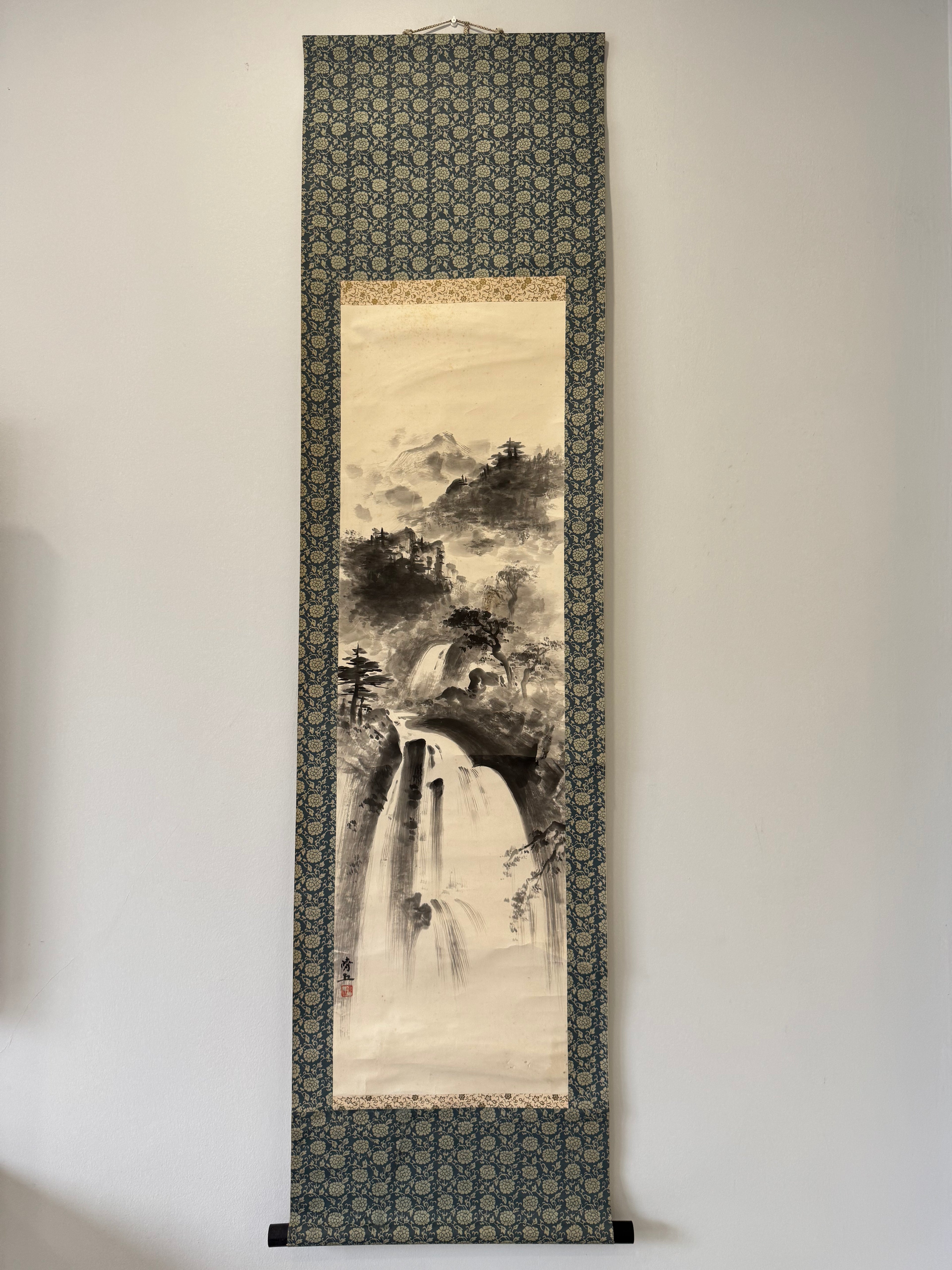 Traditional Japanese landscape scroll hanging on a wall with decorative border