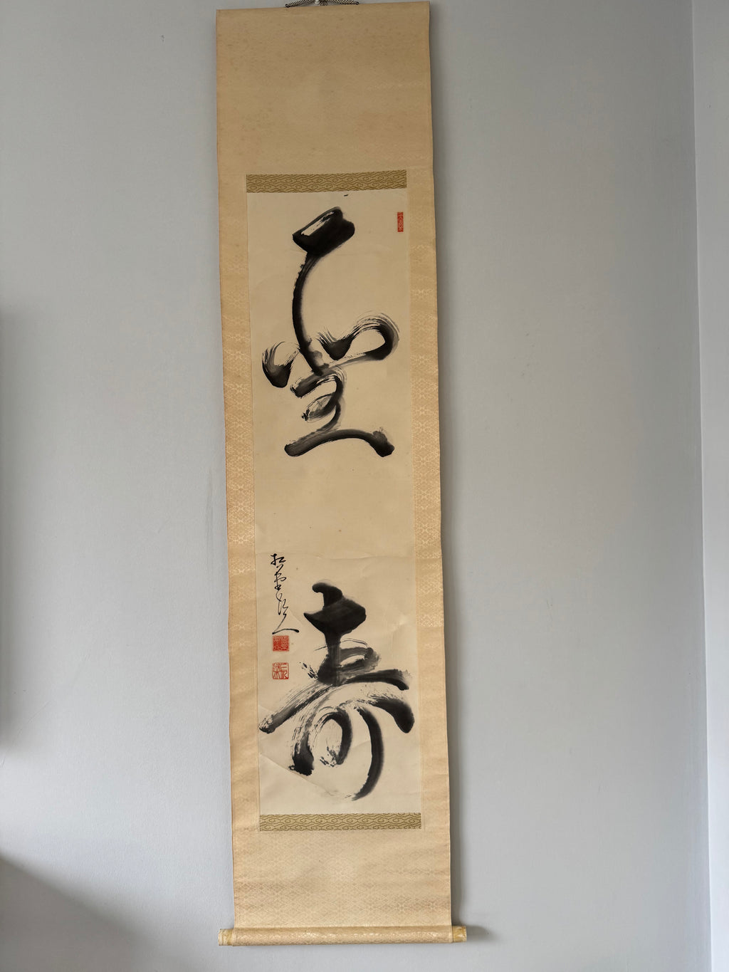 Vertical scroll with black calligraphy on beige paper against a gray background