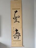 Vertical scroll with black calligraphy on beige paper against a gray background