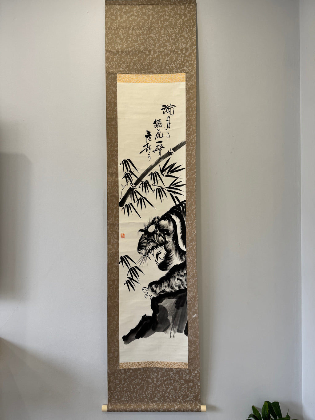 Traditional painting of a tiger and bamboo on a textured scroll against a plain wall.