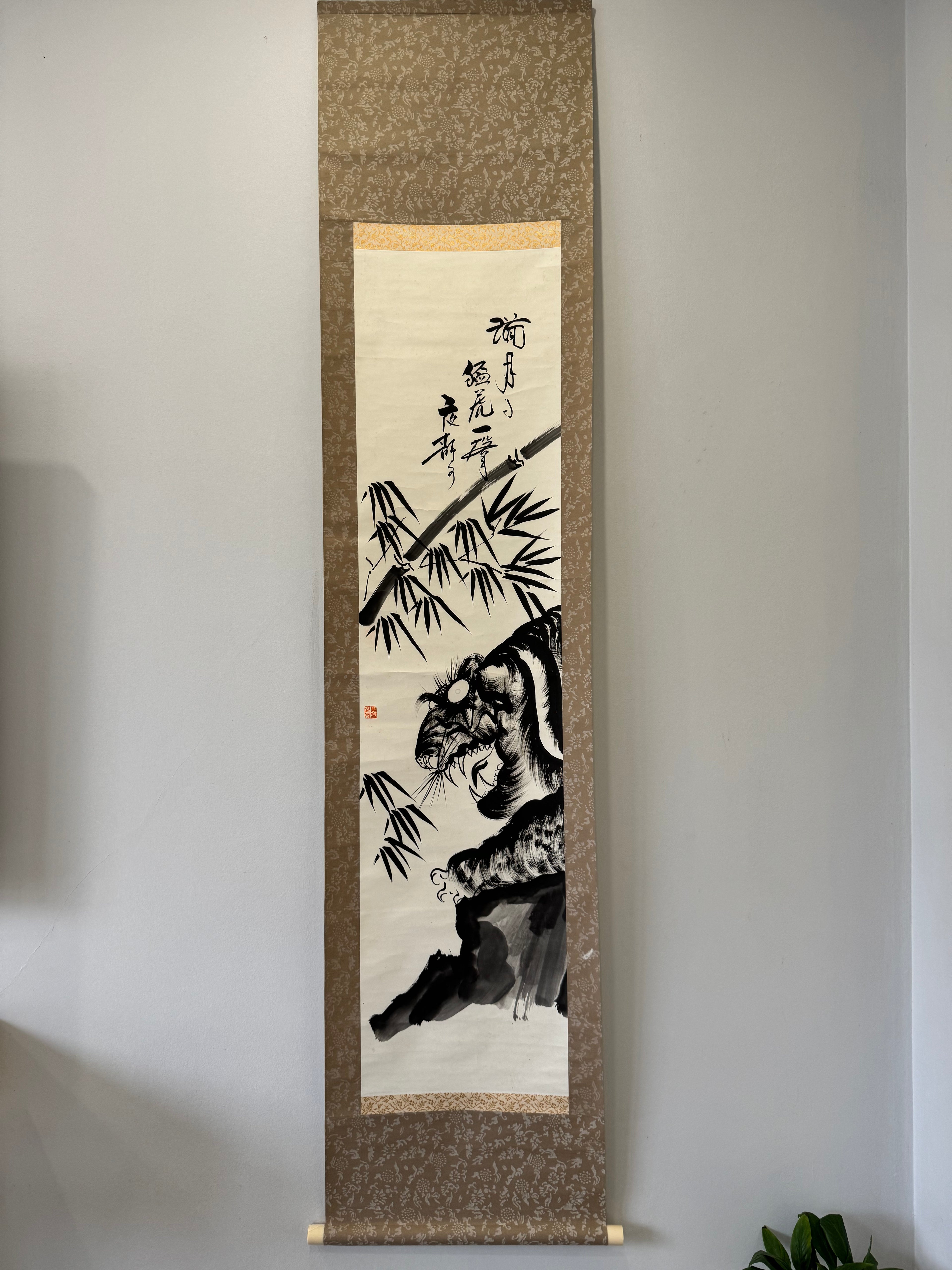 Traditional painting of a tiger and bamboo on a textured scroll against a plain wall.