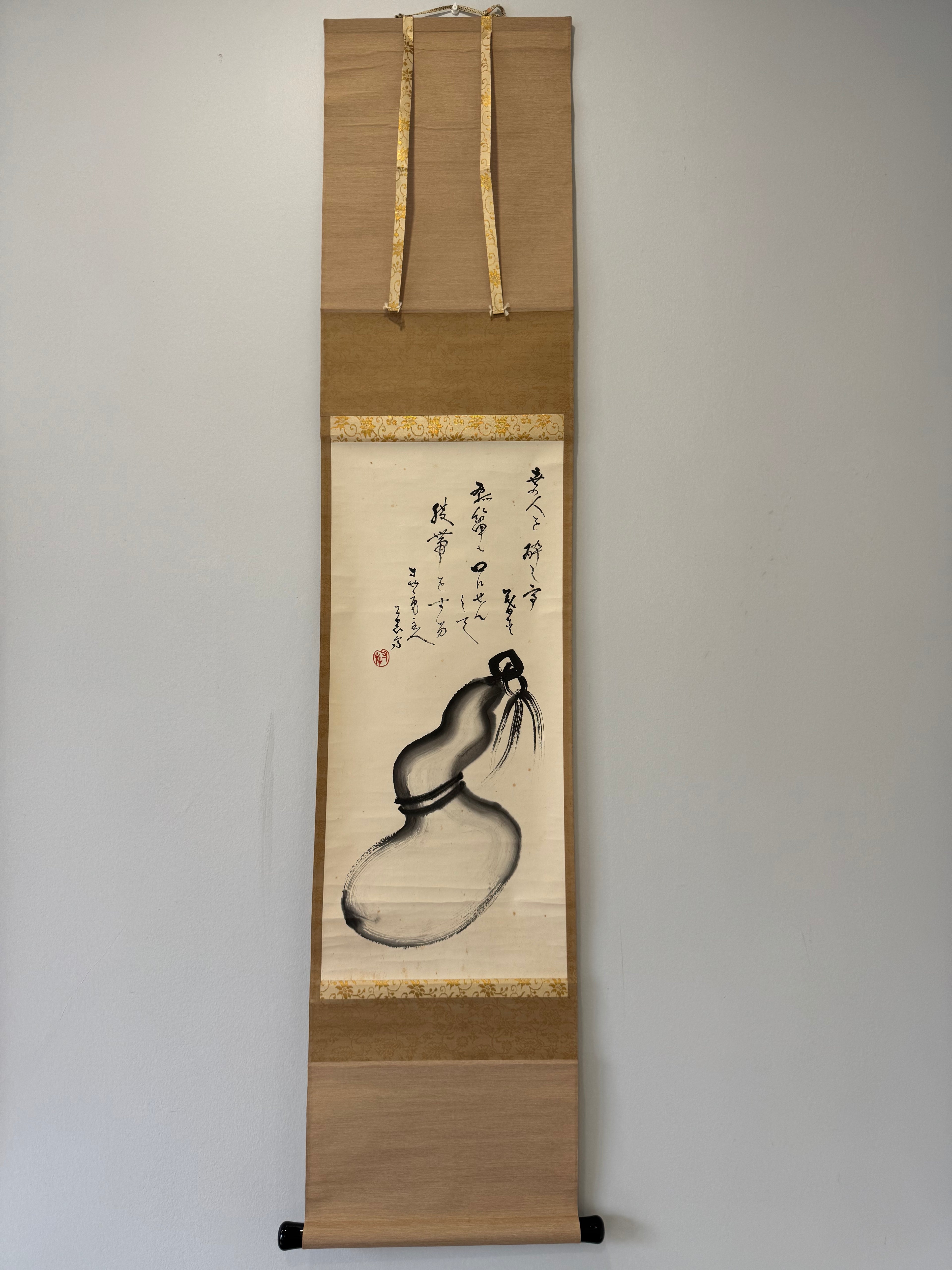 Traditional Japanese scroll with ink painting of a gourd on a plain wall.