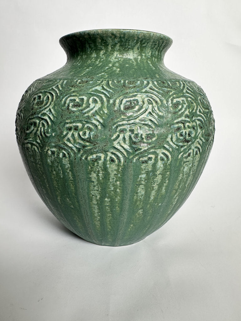 A green glazed ceramic vase with a rounded body, flared rim, and raised decorative pattern on the front, photographed against a plain light background.
