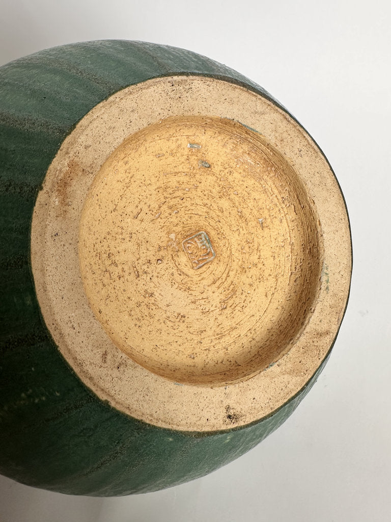 Close-up of the bottom of a ceramic vase or planter, showing a dark green glazed exterior and a light tan unglazed circular base on a plain white background.