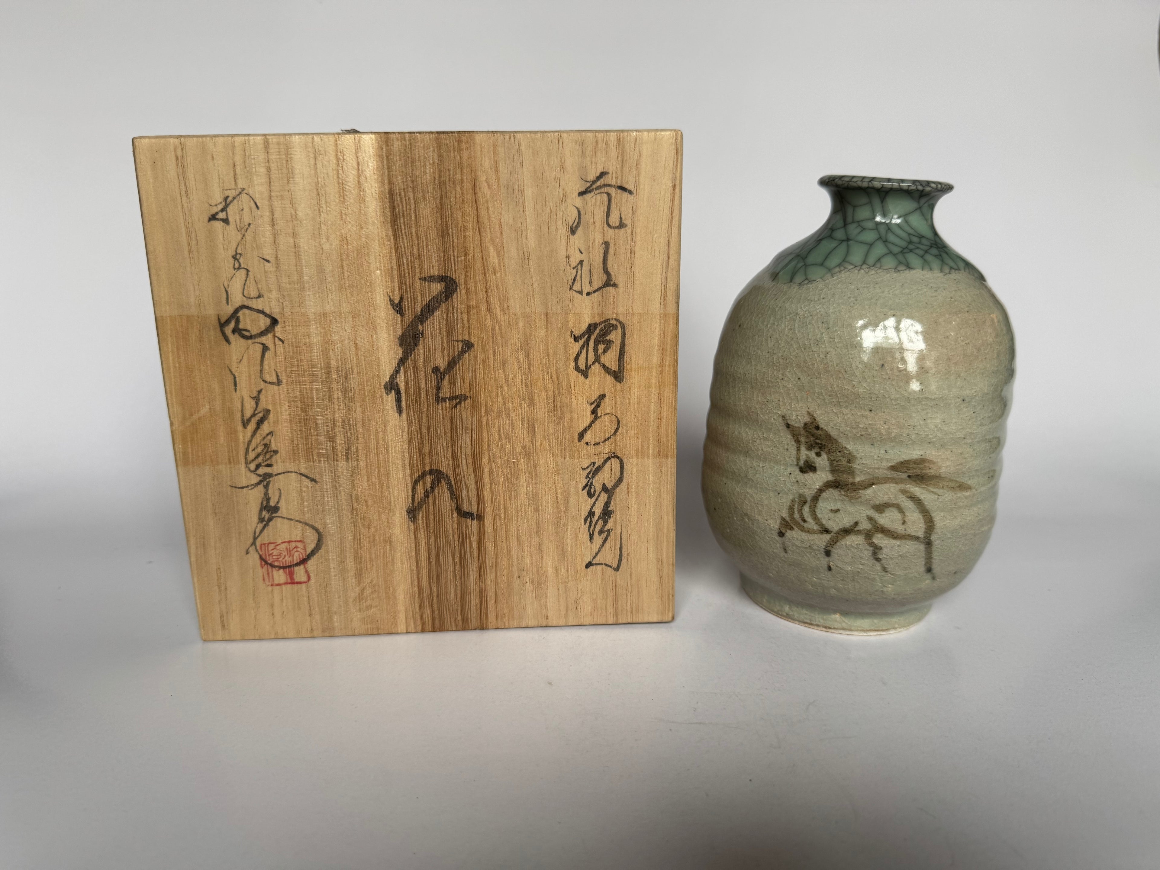 Wooden box with calligraphy and a ceramic vase with horse design on a white background