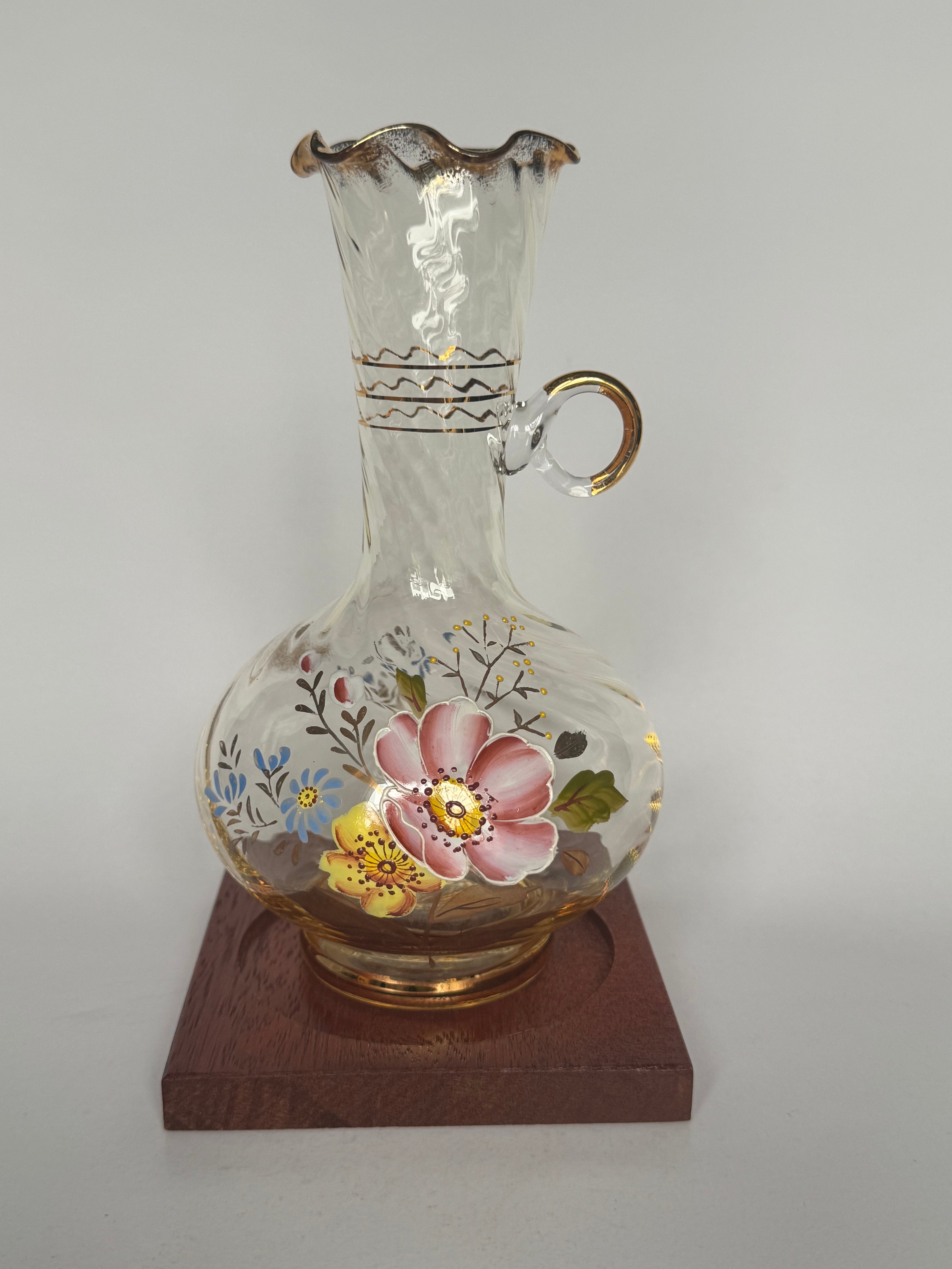 Decorative glass vase with floral designs on a wooden stand against a plain background