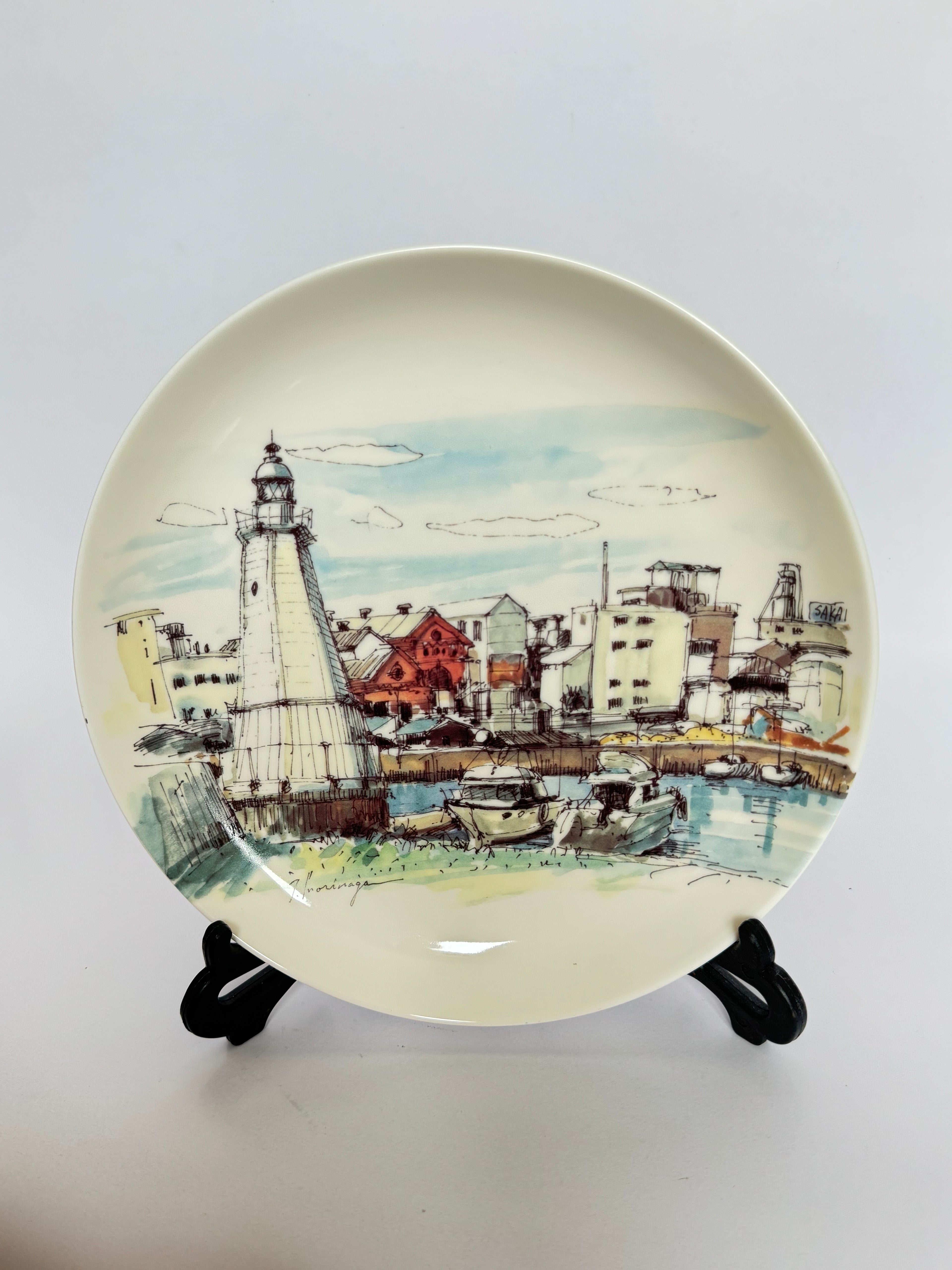 Decorative plate with a lighthouse and harbor scene on a white background