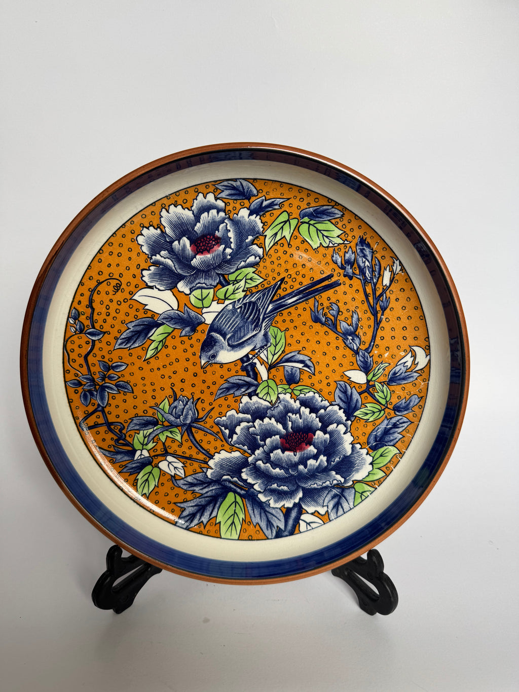 Decorative plate with floral and bird design on a stand against a white background
