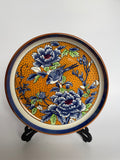 Decorative plate with floral and bird design on a stand against a white background