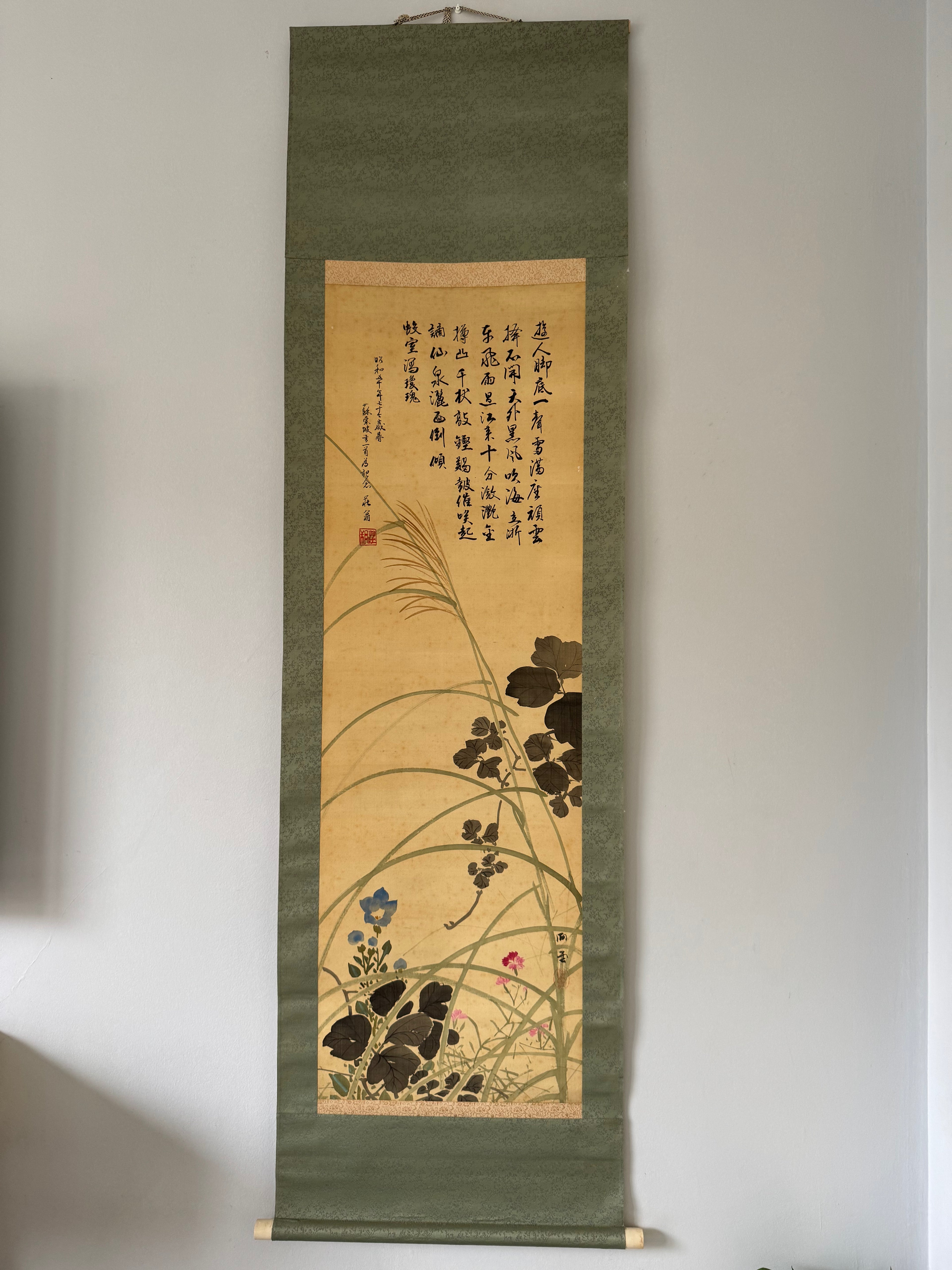Floral and calligraphy artwork on a green scroll against a plain wall.