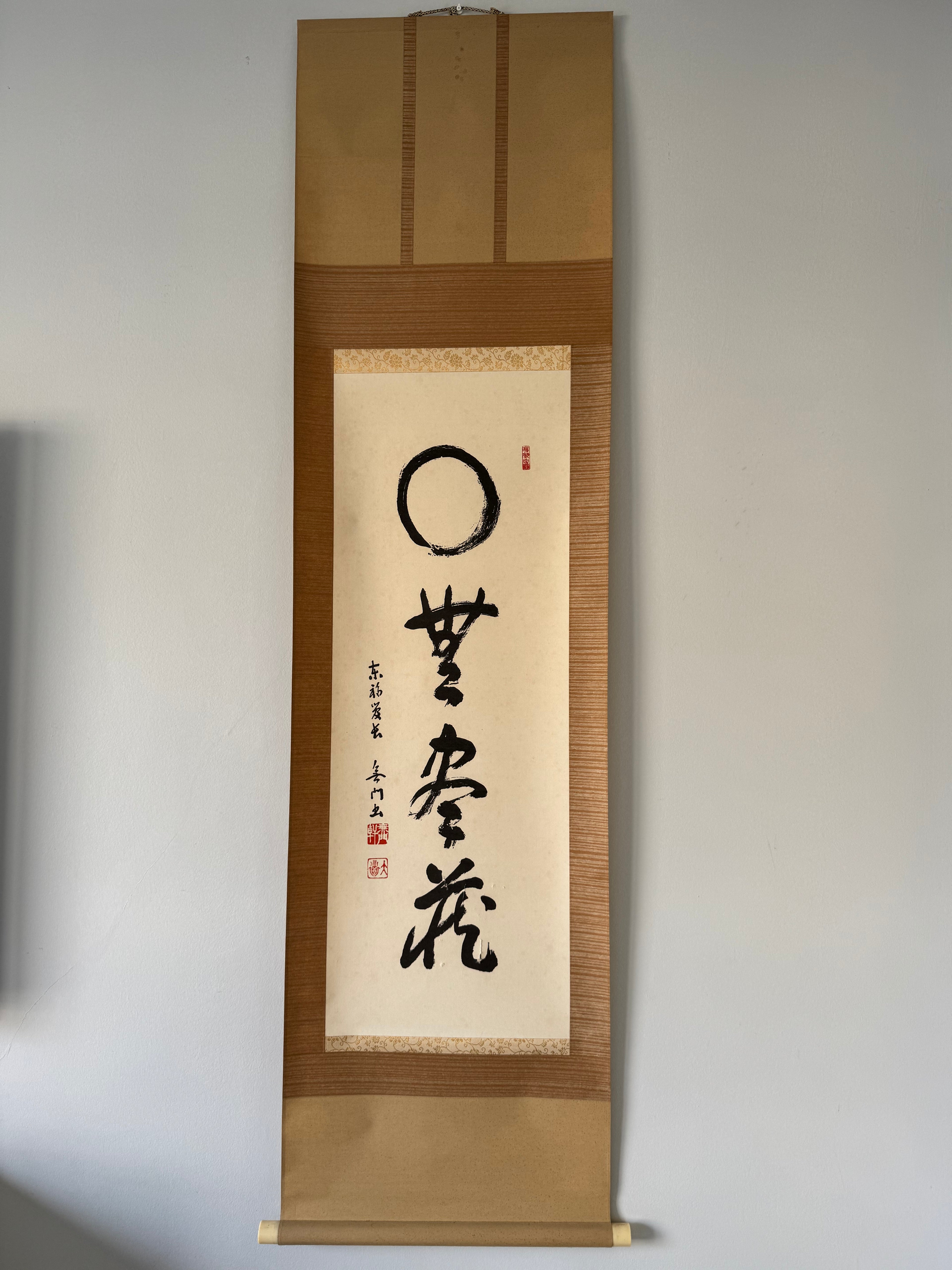 Traditional Japanese calligraphy scroll on a wooden frame against a plain wall.