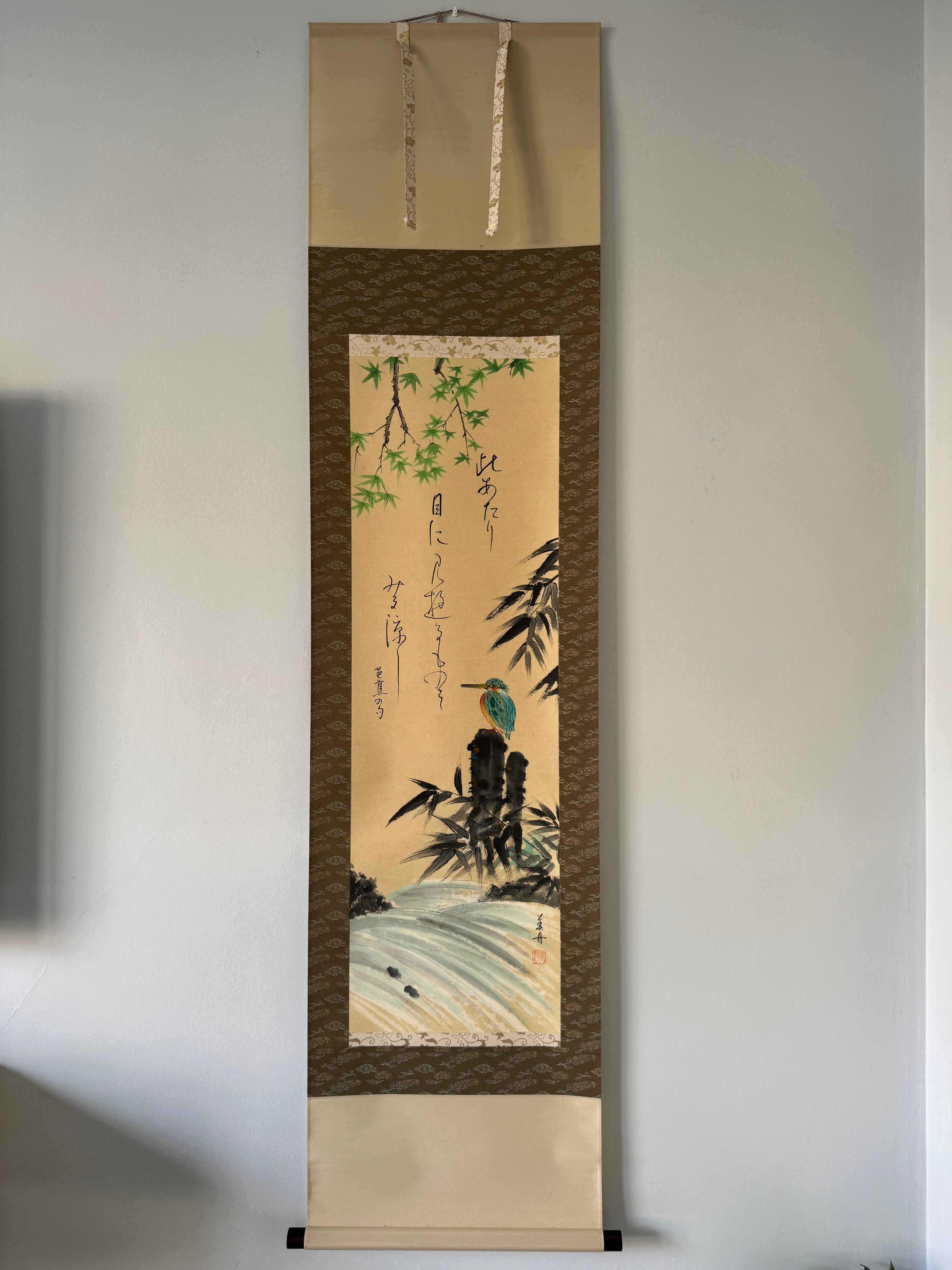 Traditional Japanese scroll with a bird and bamboo design on a plain wall.