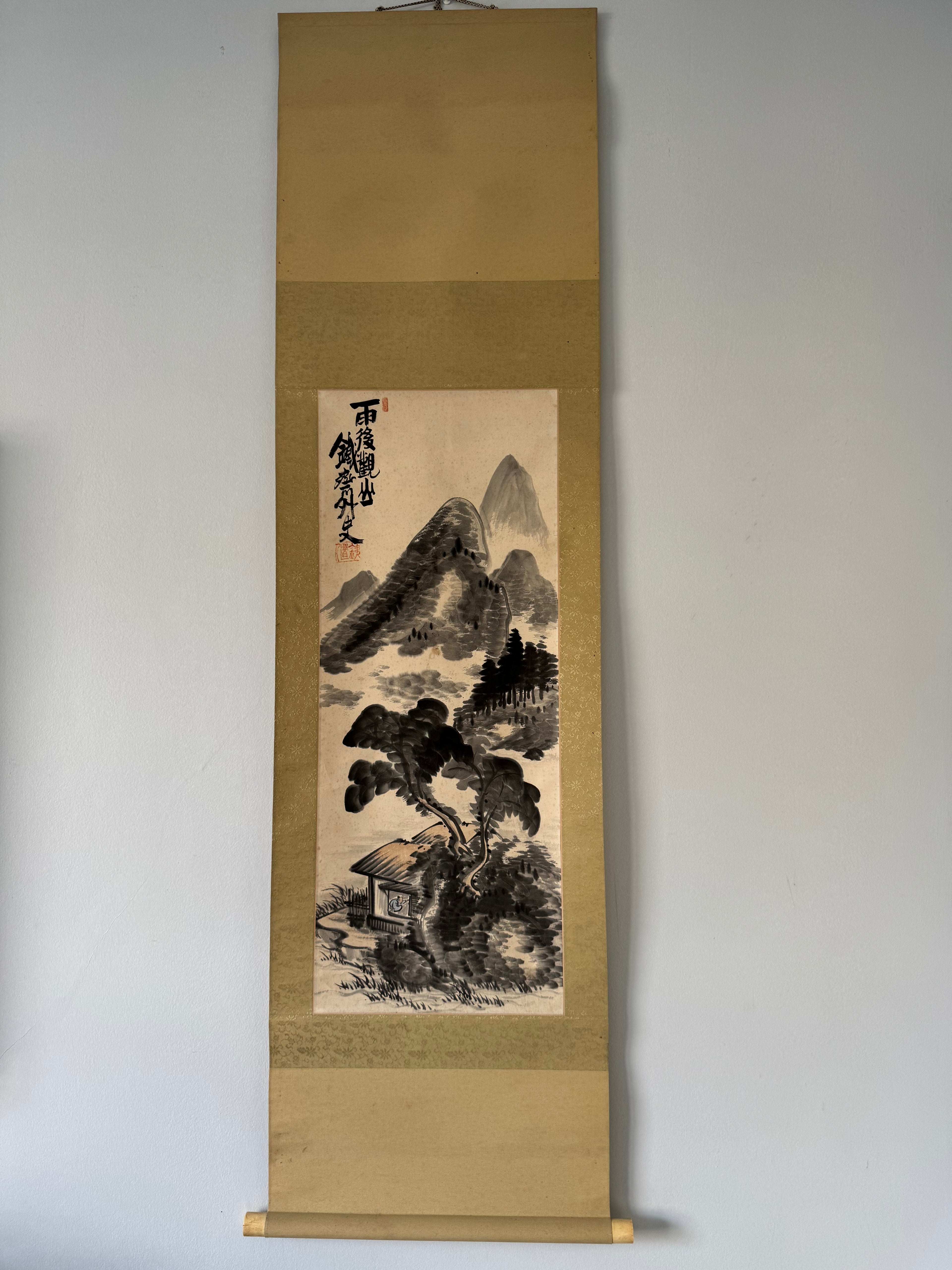 Traditional Japanes landscape painting on a vertical scroll against a plain wall.
