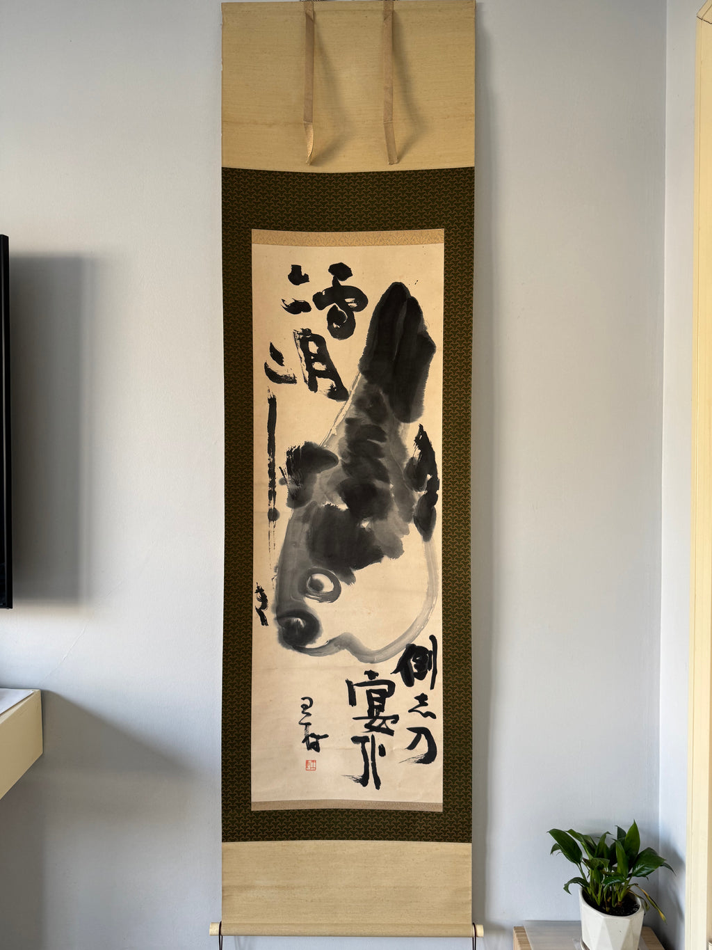 Traditional Japanese artwork with a fish design and calligraphy on a stand against a plain wall.