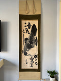 Traditional Japanese artwork with a fish design and calligraphy on a stand against a plain wall.