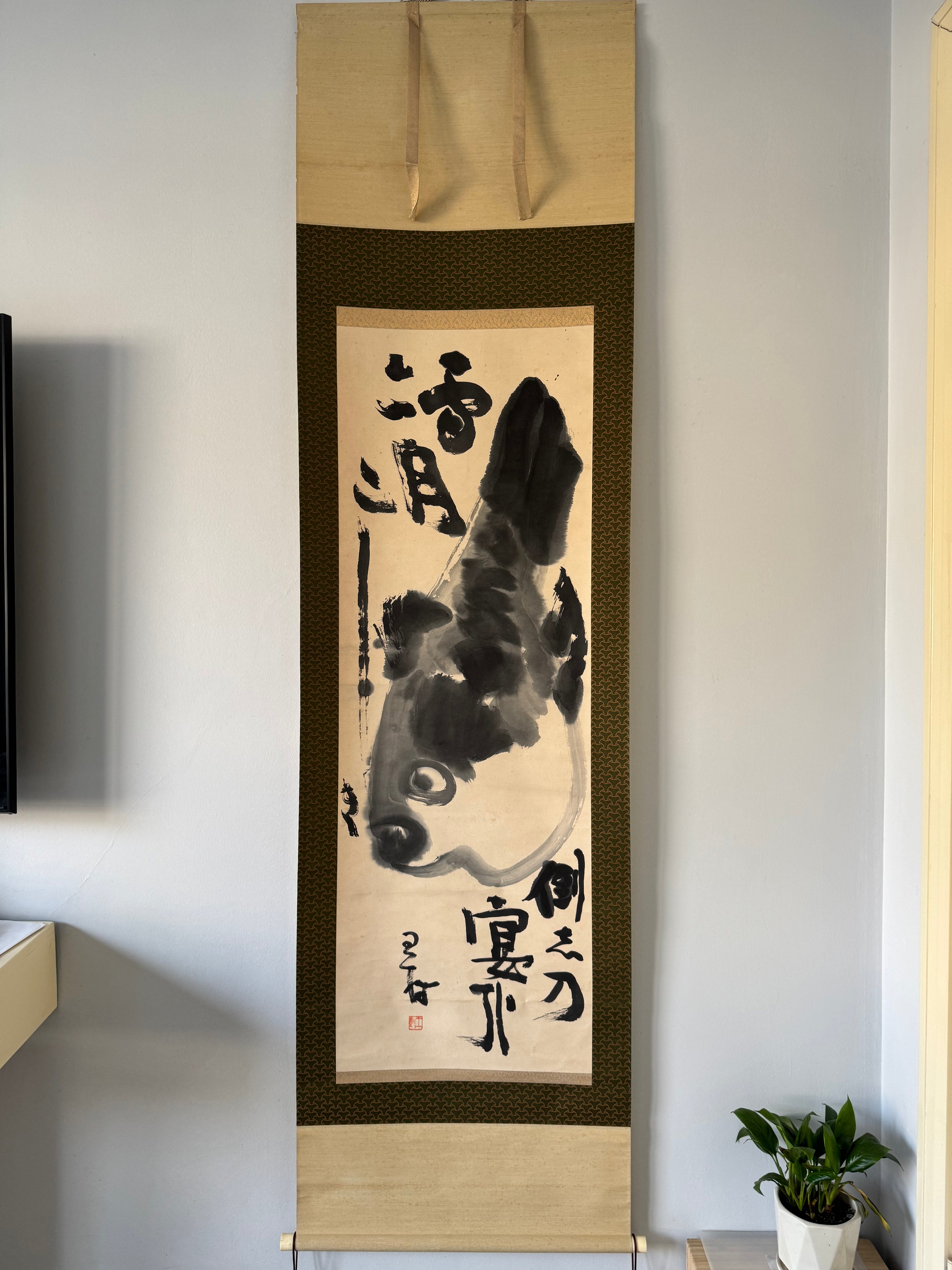Traditional Japanese artwork with a fish design and calligraphy on a stand against a plain wall.