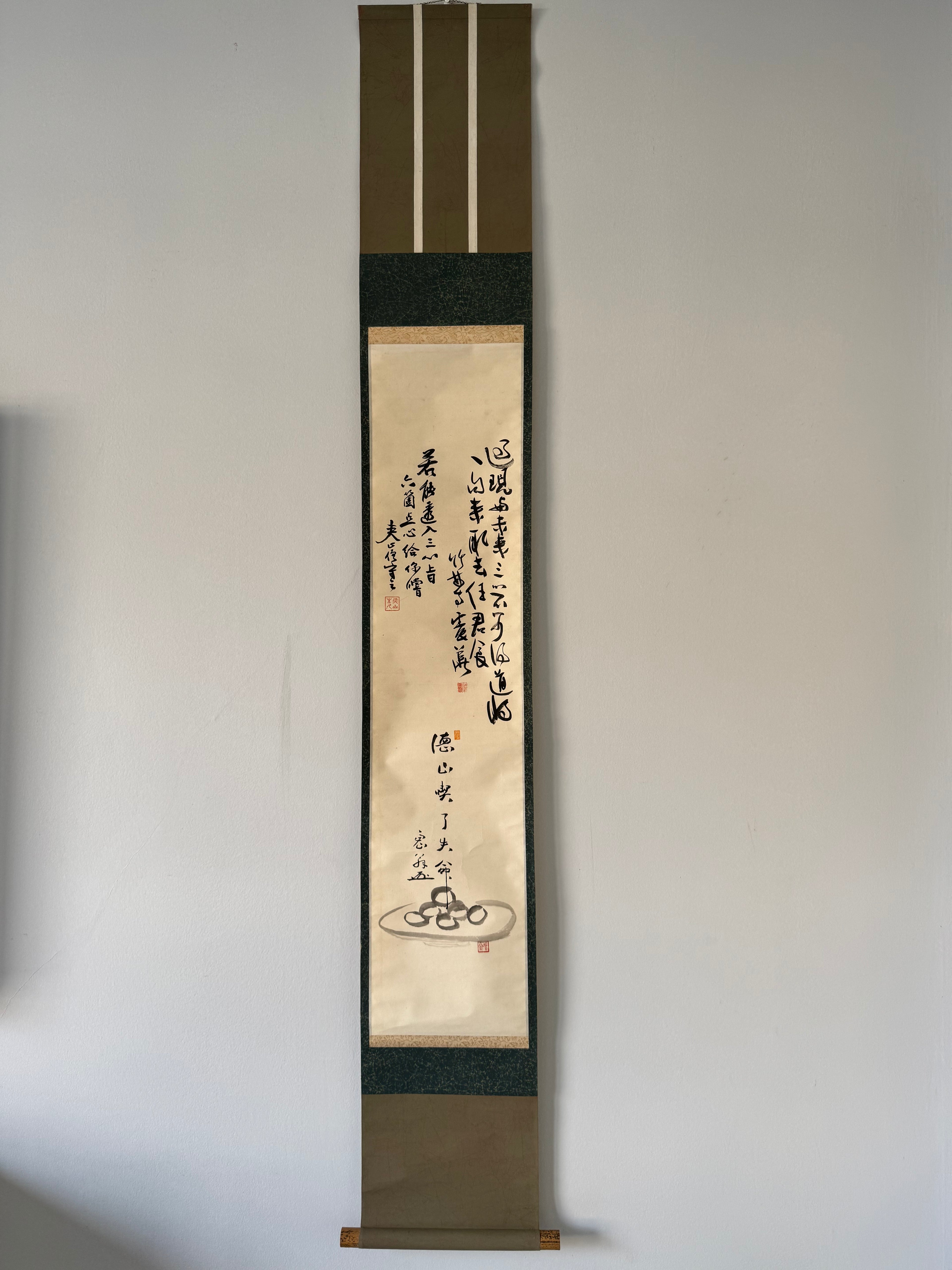 Vertical scroll with calligraphy and a small illustration on a plain wall