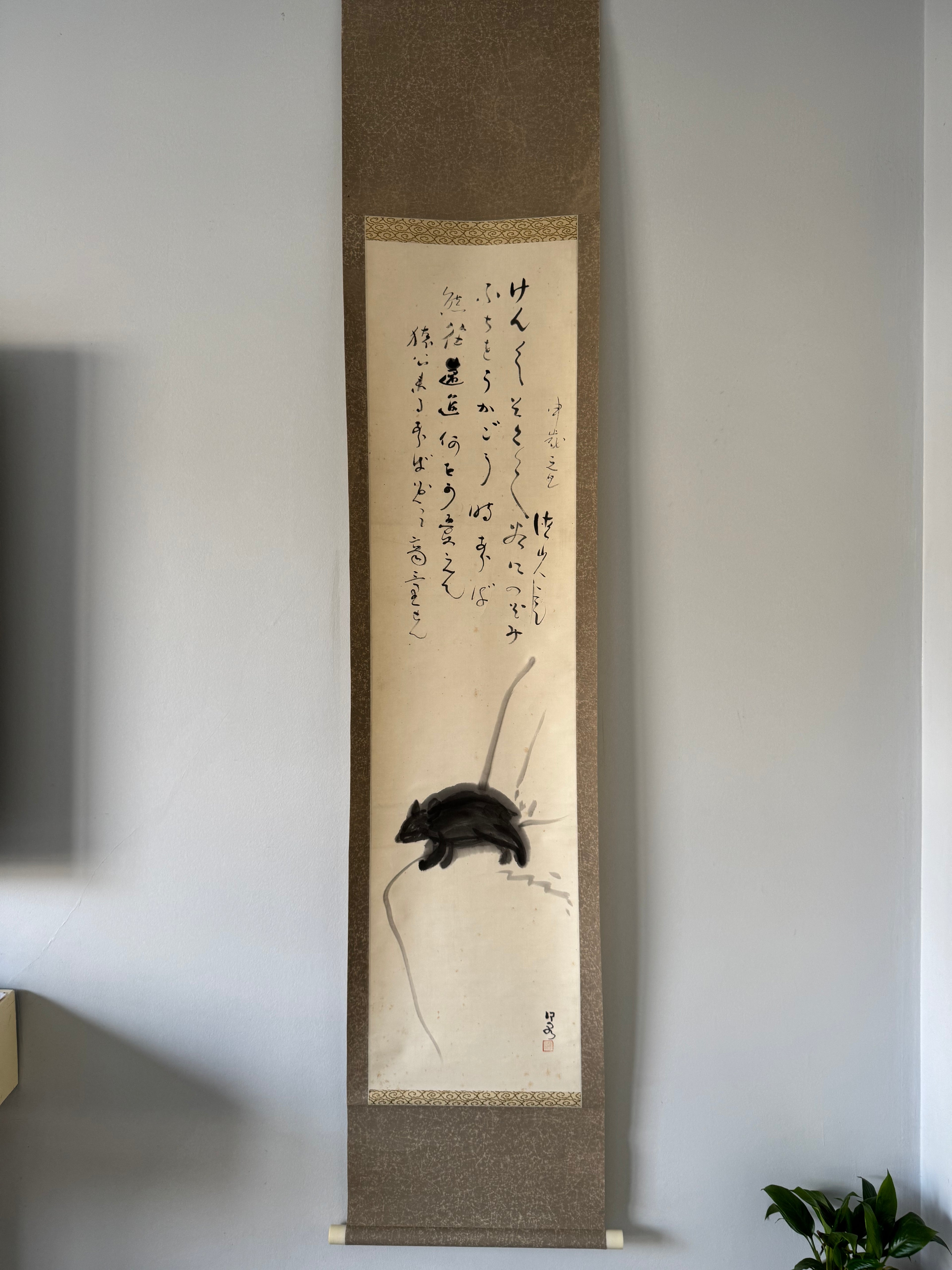 Traditional Japanese scroll with calligraphy and a mouse illustration on a plain wall.