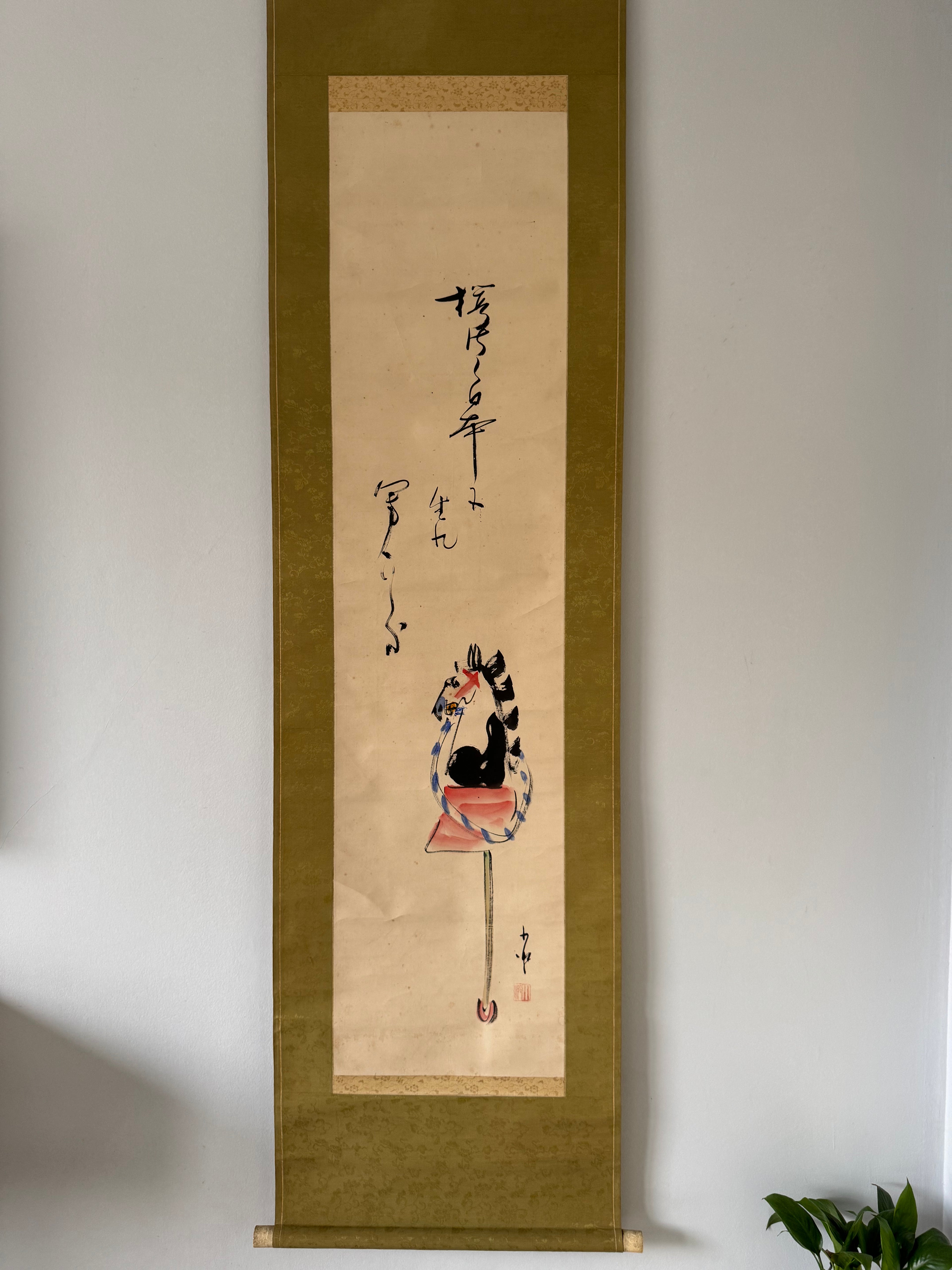 Traditional Japanese scroll with calligraphy and illustration on a plain wall.
