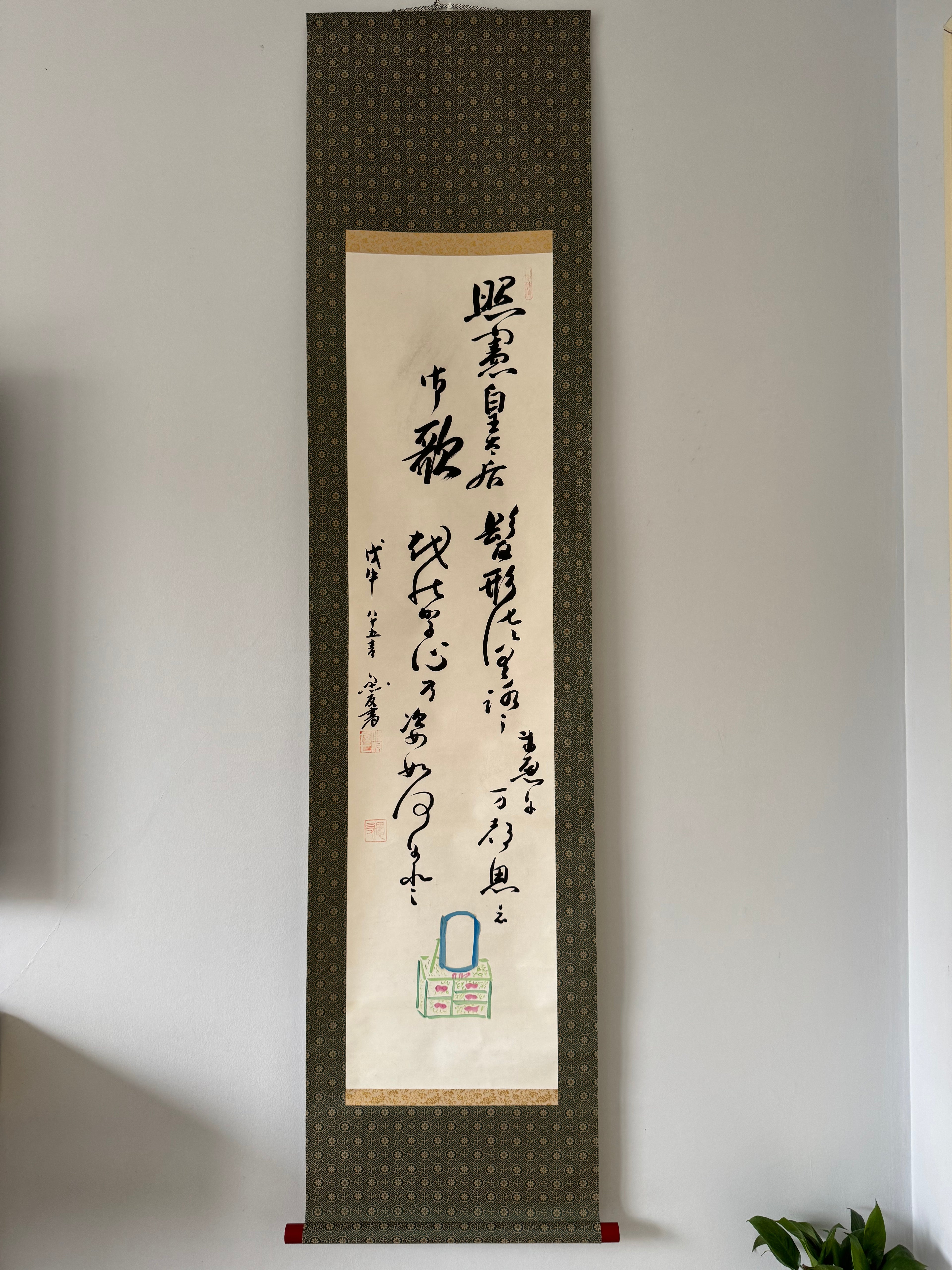 Vertical scroll with calligraphy on a plain wall