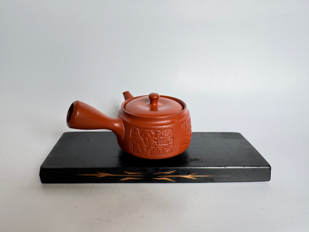 Red ceramic teapot on a black stand with a white background