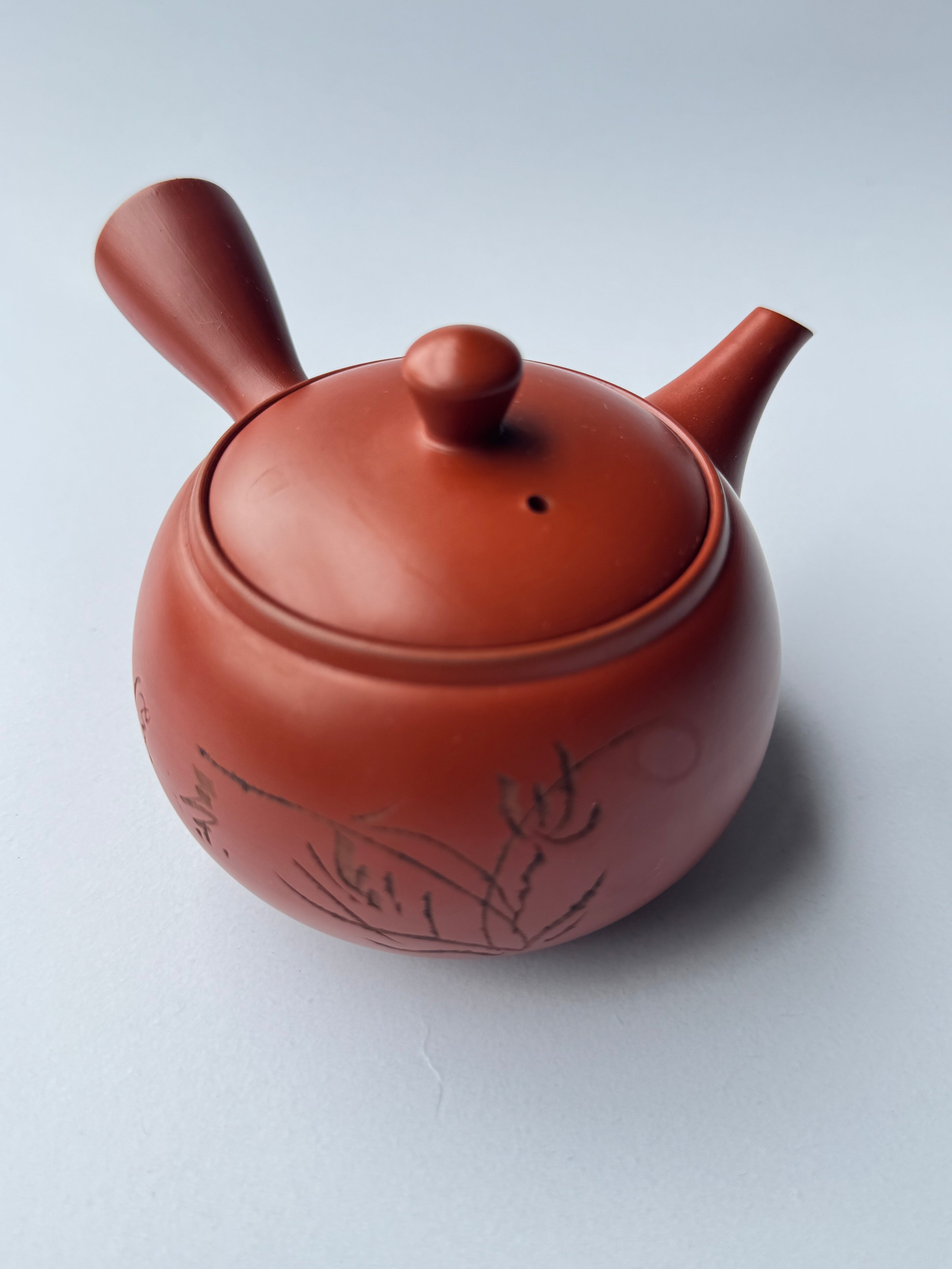 Red ceramic teapot with lid on a light gray background