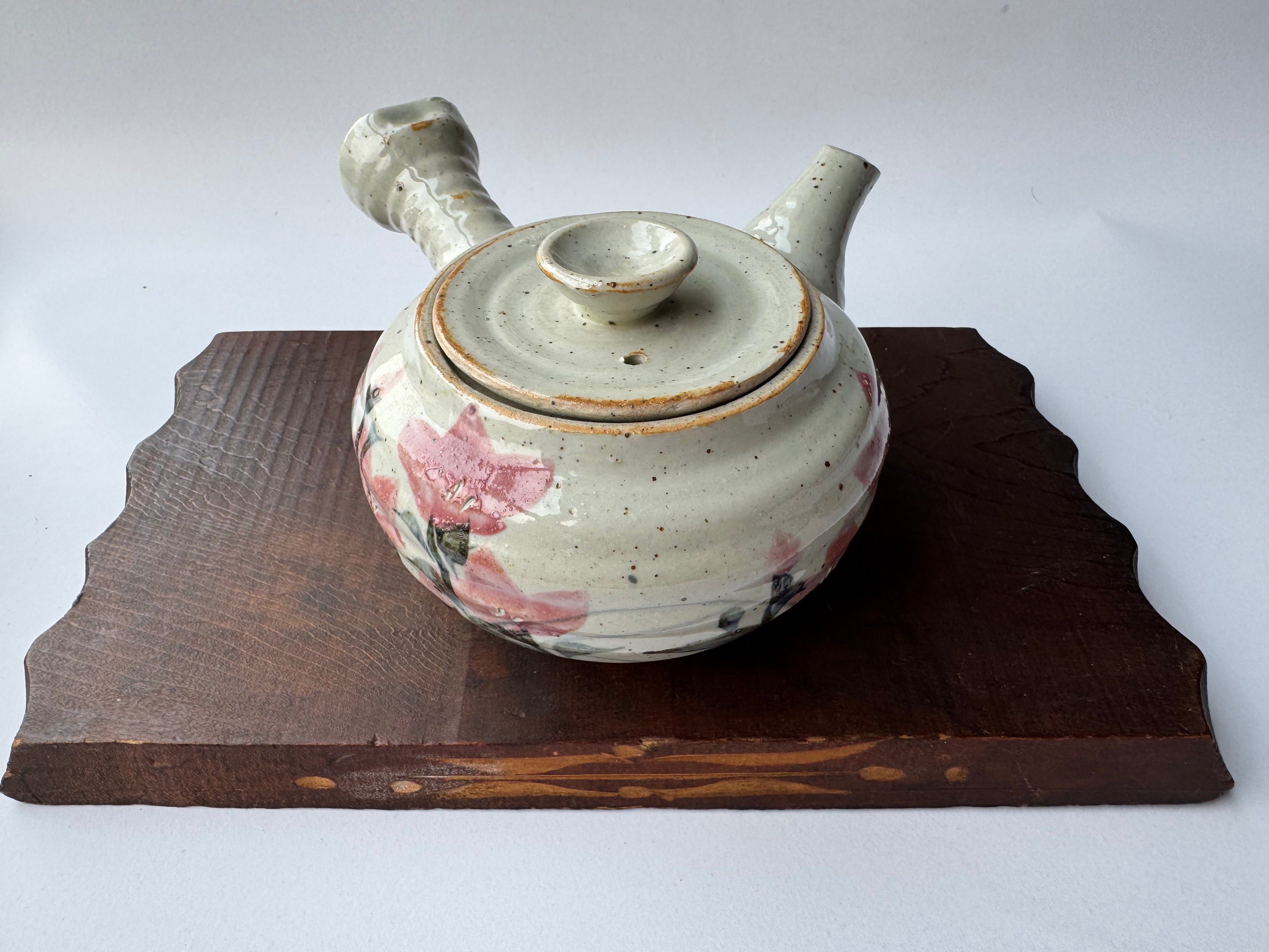 Ceramic teapot with floral designs on a wooden stand against a white background