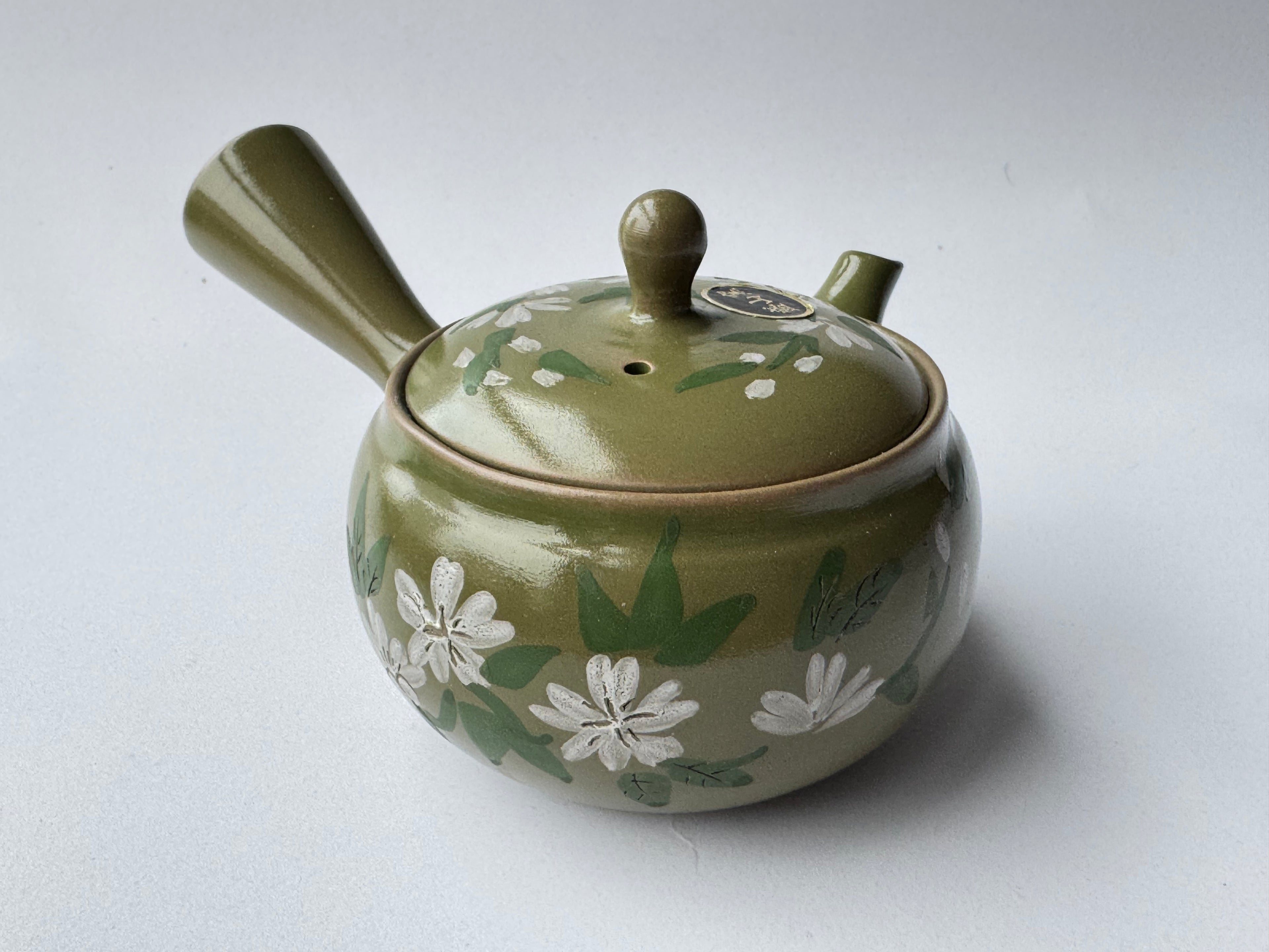 Green ceramic teapot with floral patterns on a white background